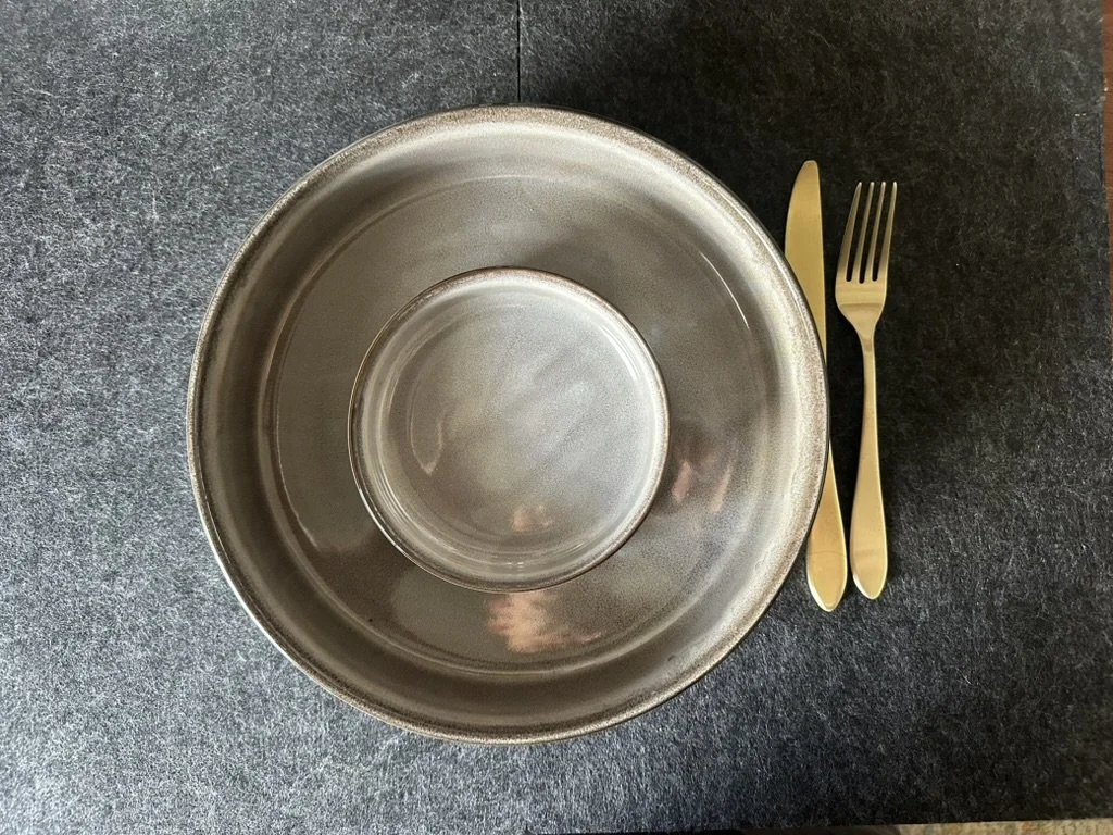 An overhead view of a large metallic bowl with a smaller metallic bowl inside it, placed on a dark countertop, with gold-colored knife and fork set beside the bowls.
