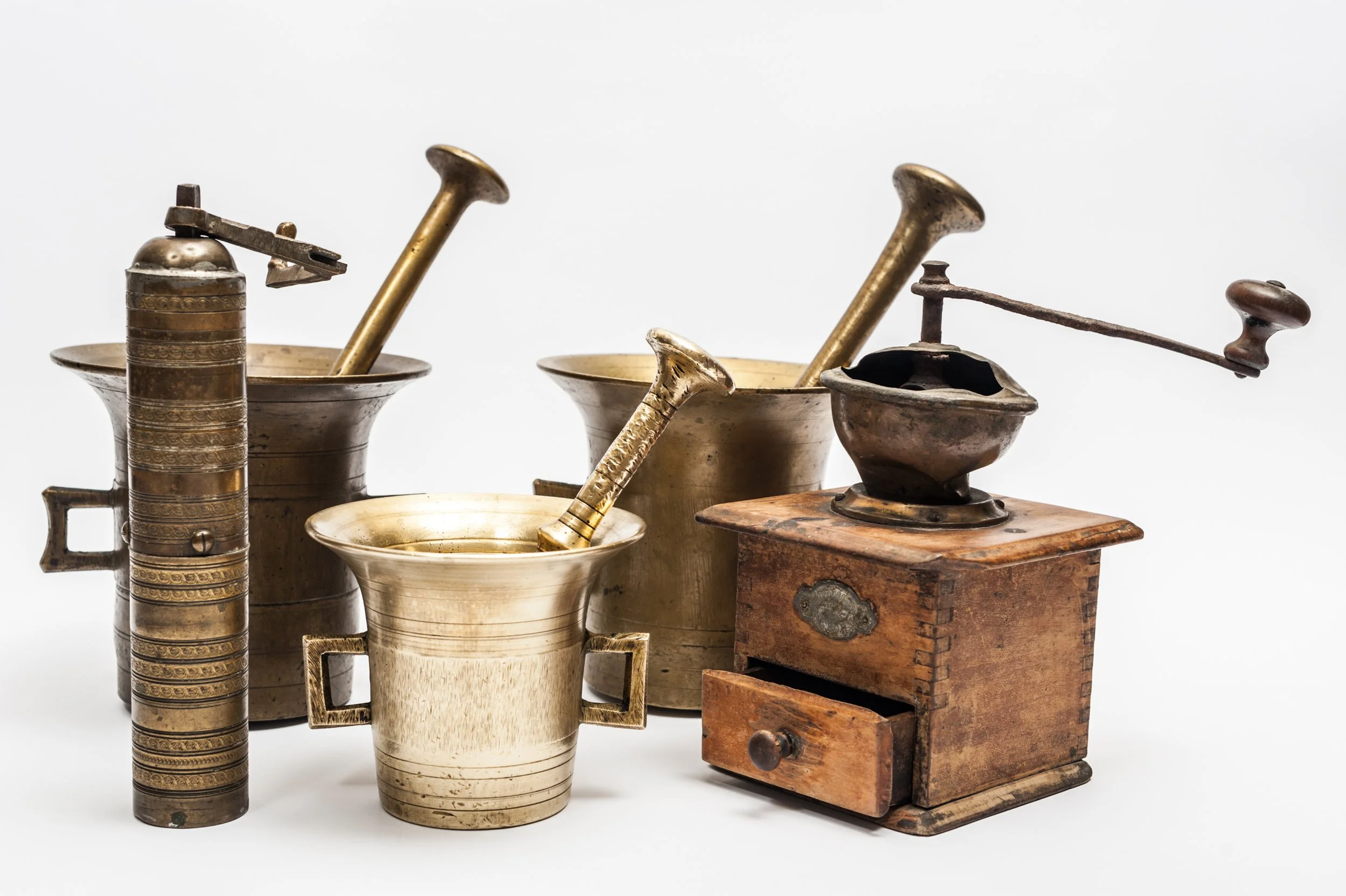 Collection of vintage kitchen tools, including brass and ceramic grinders and a wooden box with a drawer.