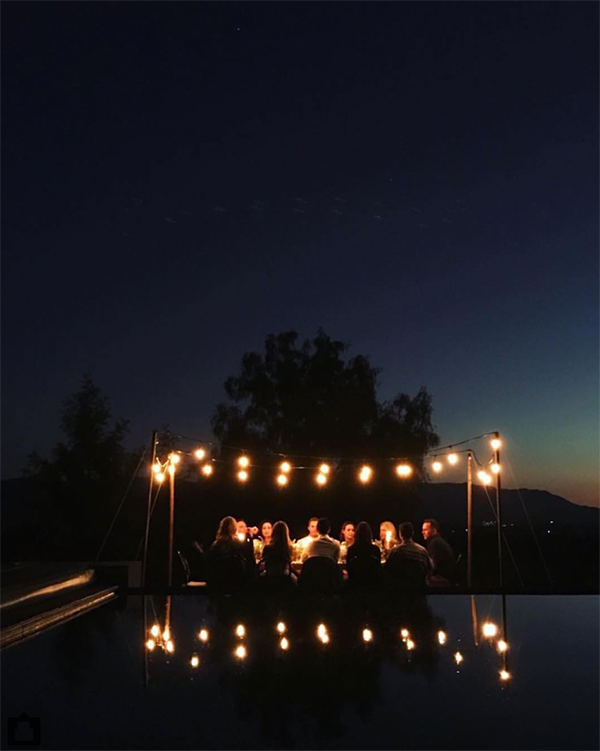 People sitting at a table under string lights outdoors at night, with a dark sky and trees in the background.