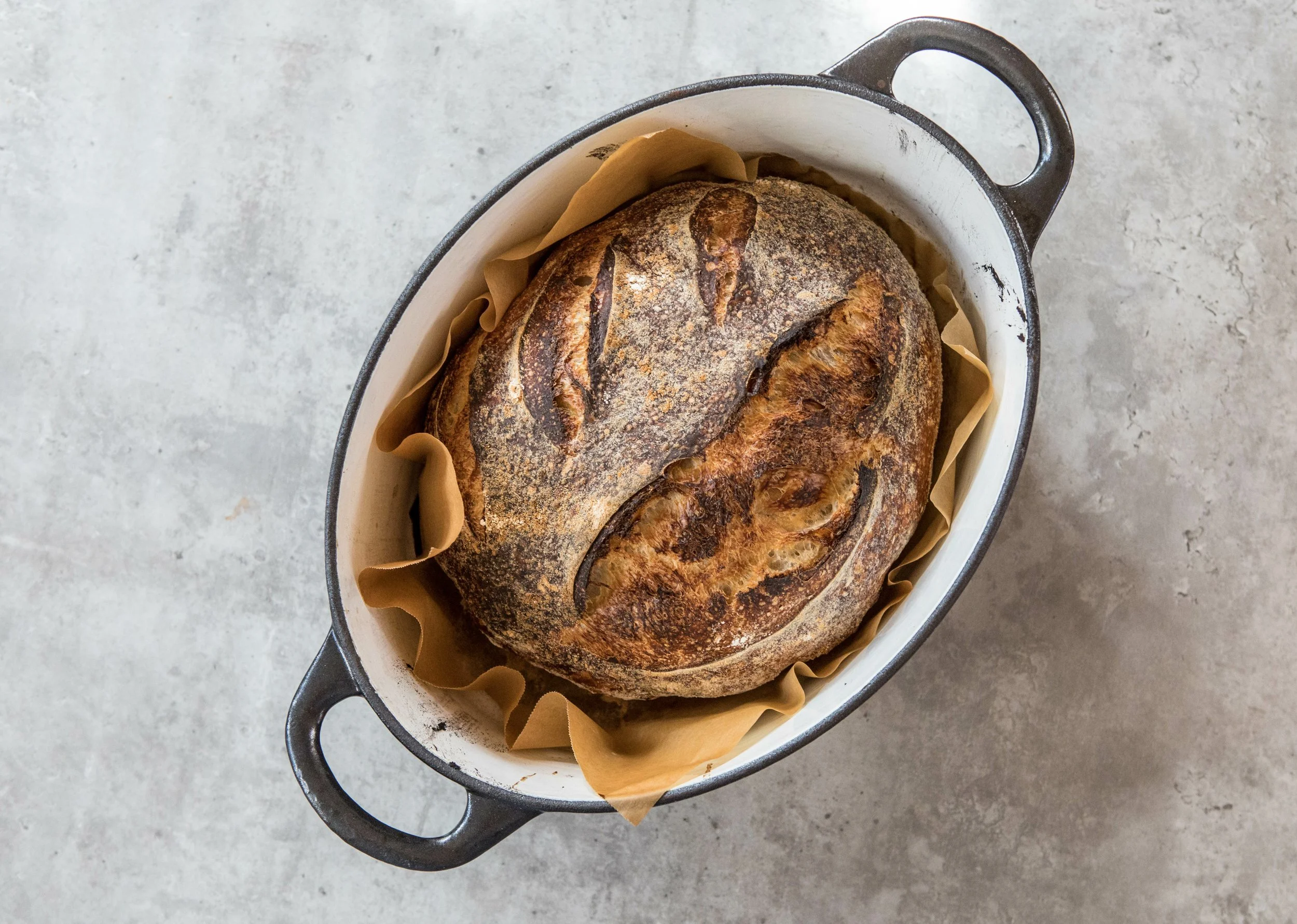 A loaf of freshly baked bread in a baking dish on a light gray surface.