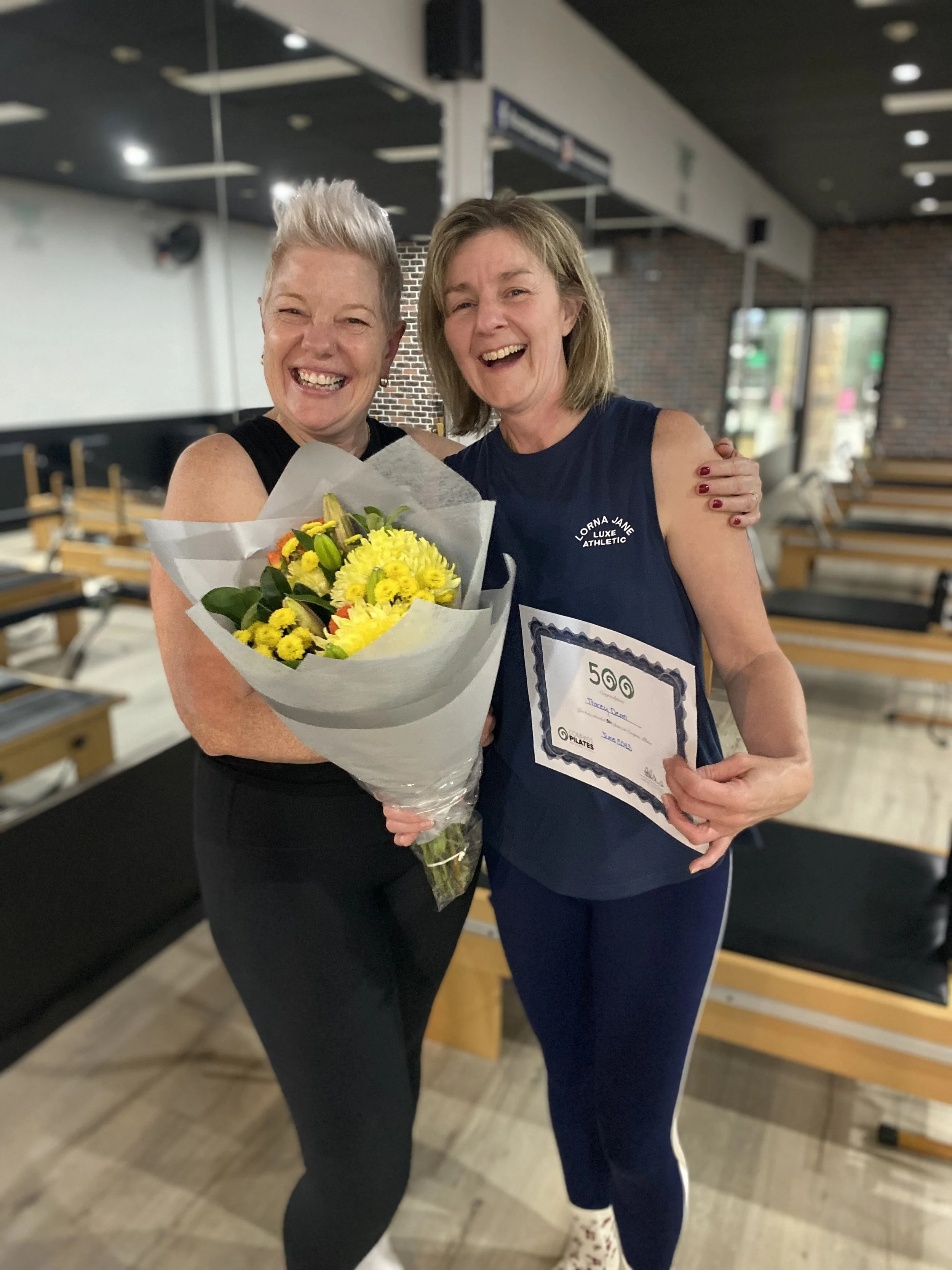 Two women smiling with flowers and certificate