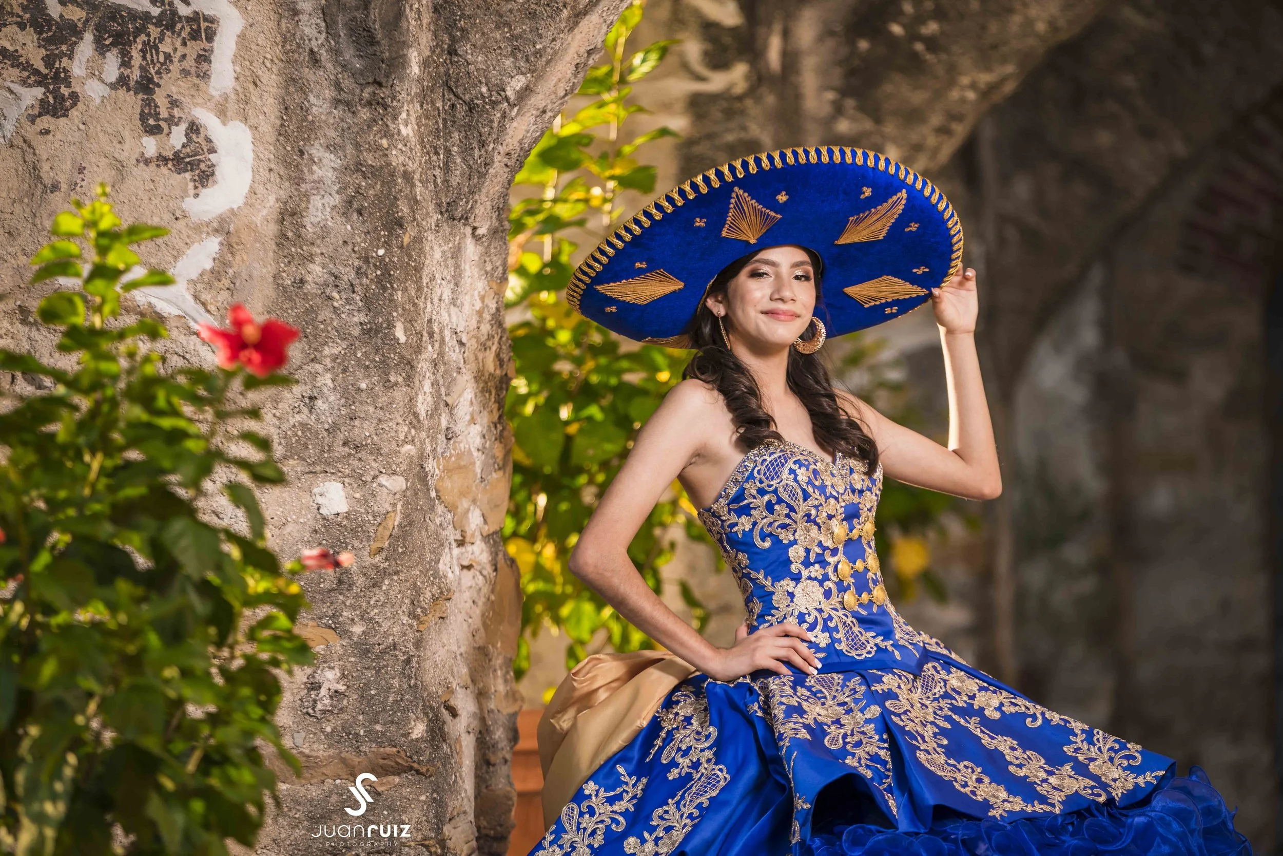 a quinceañera in a charro dress with a hat. quinceañera in a blue dress, with golden colors