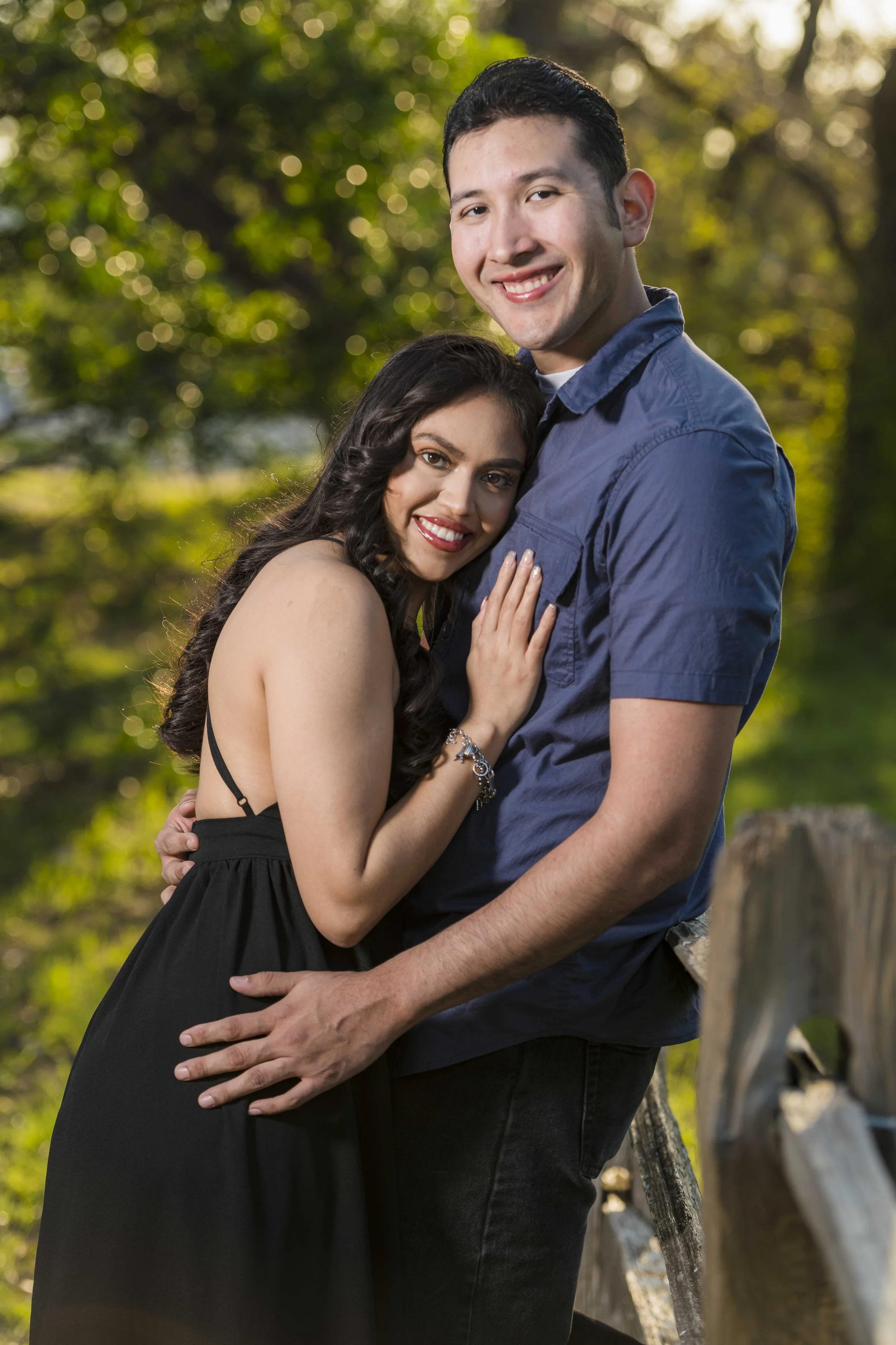 A young couple hugging outdoors, with trees and sunlight in the background.