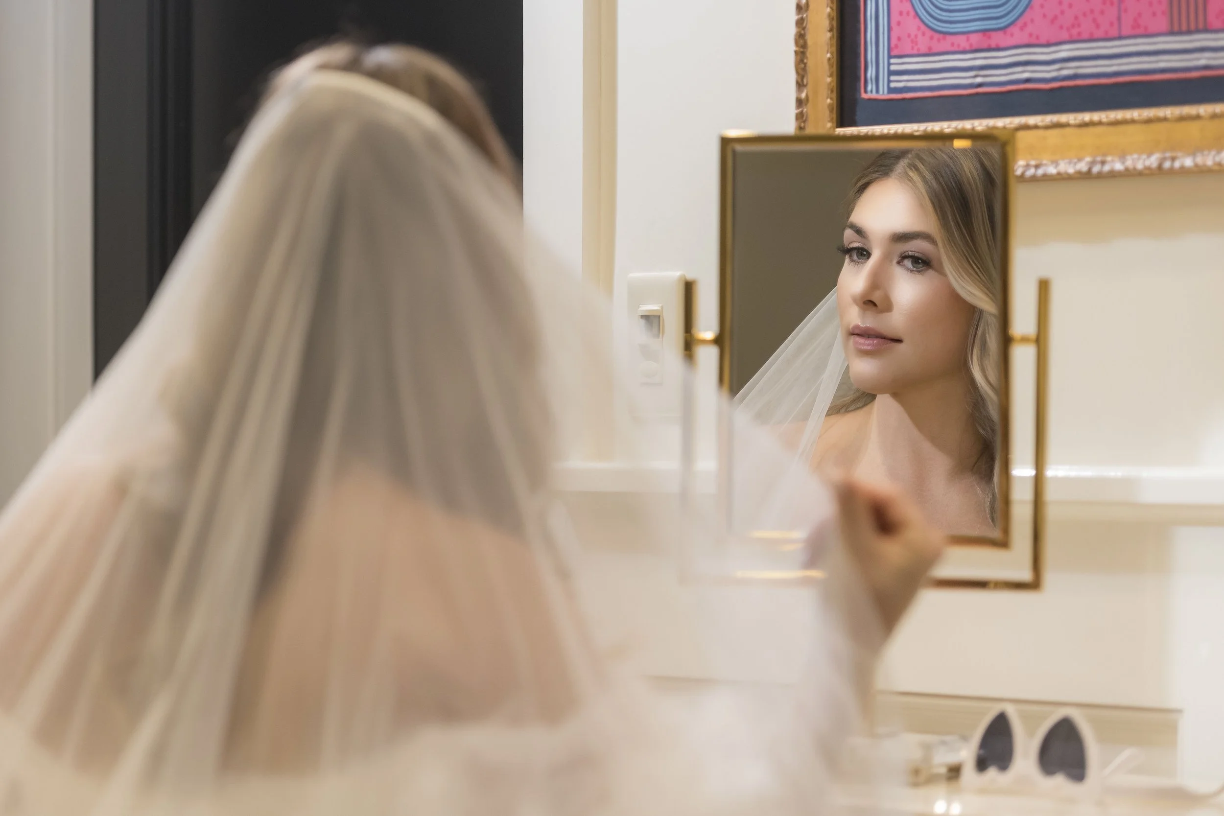 Bride looking at herself in a mirror, wearing a veil.