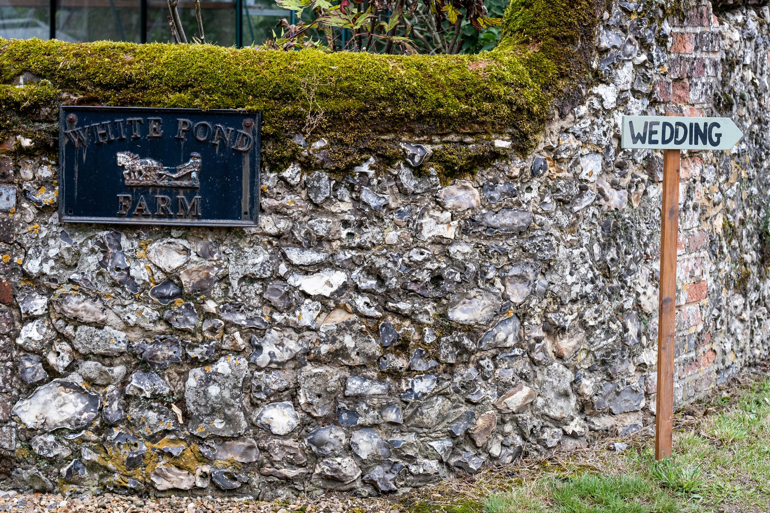 Cobbled wall with a sign saying White Pond Farm, another sign attached to a post saying wedding.