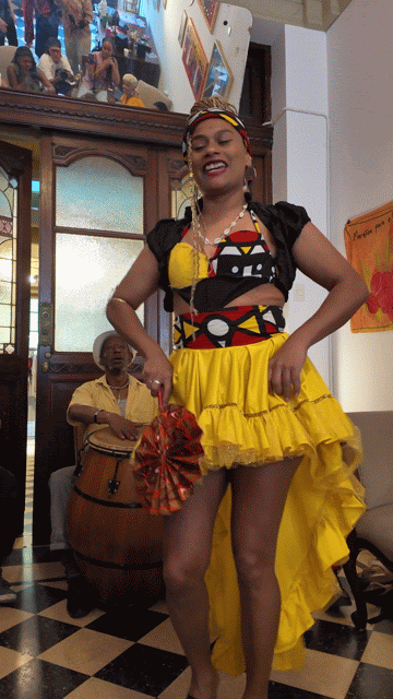 Smiling Black woman with braids wearing beige sunglasses in front of a colorful building in Buenos Aires, Argentina 