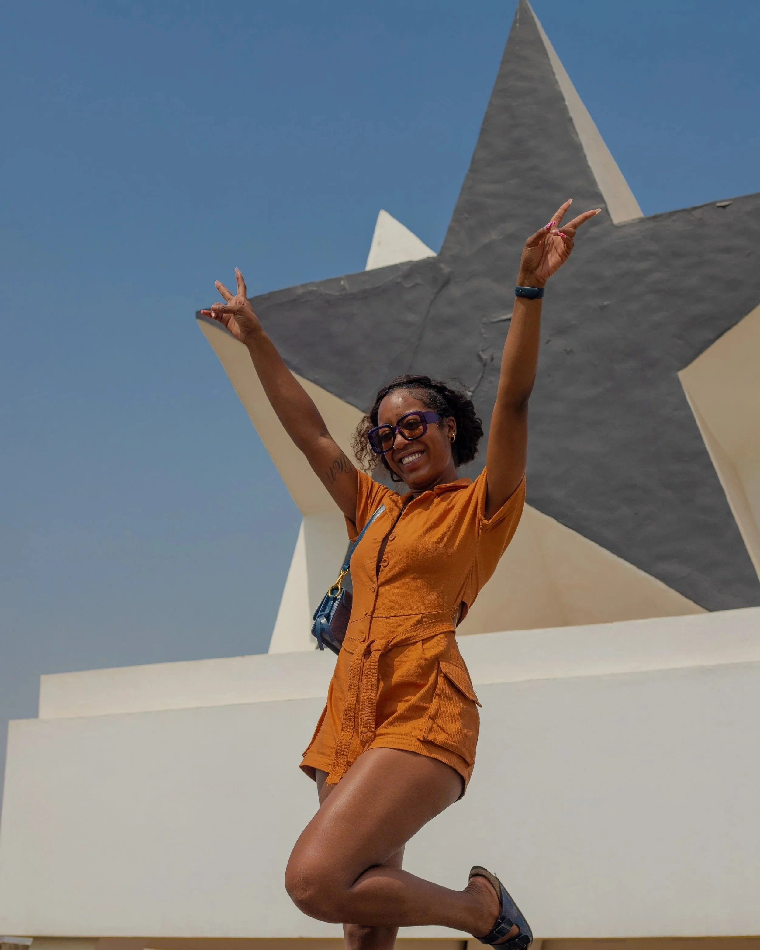 Smiling Black woman wearing sunglasses weaving Ghana's flag in front of Black Star Square in Accra, Ghana