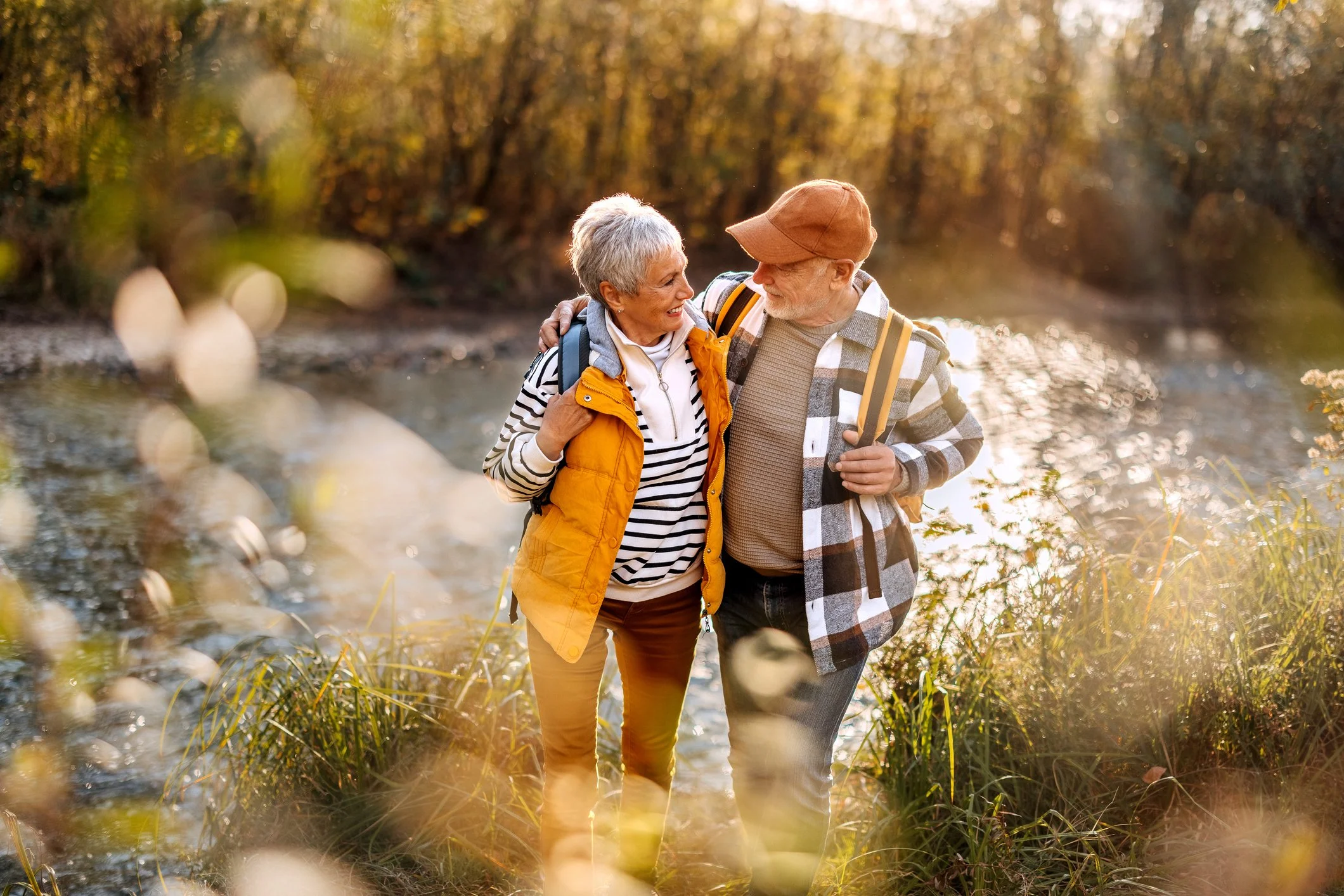 A senior couple hiking by a river during autumn, smiling and enjoying each other's company.