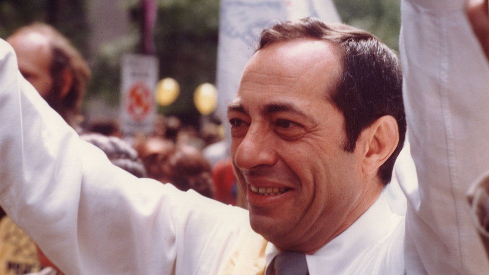 photo of Mario Cuomo raising his arms and smiling, with a crowd in the background