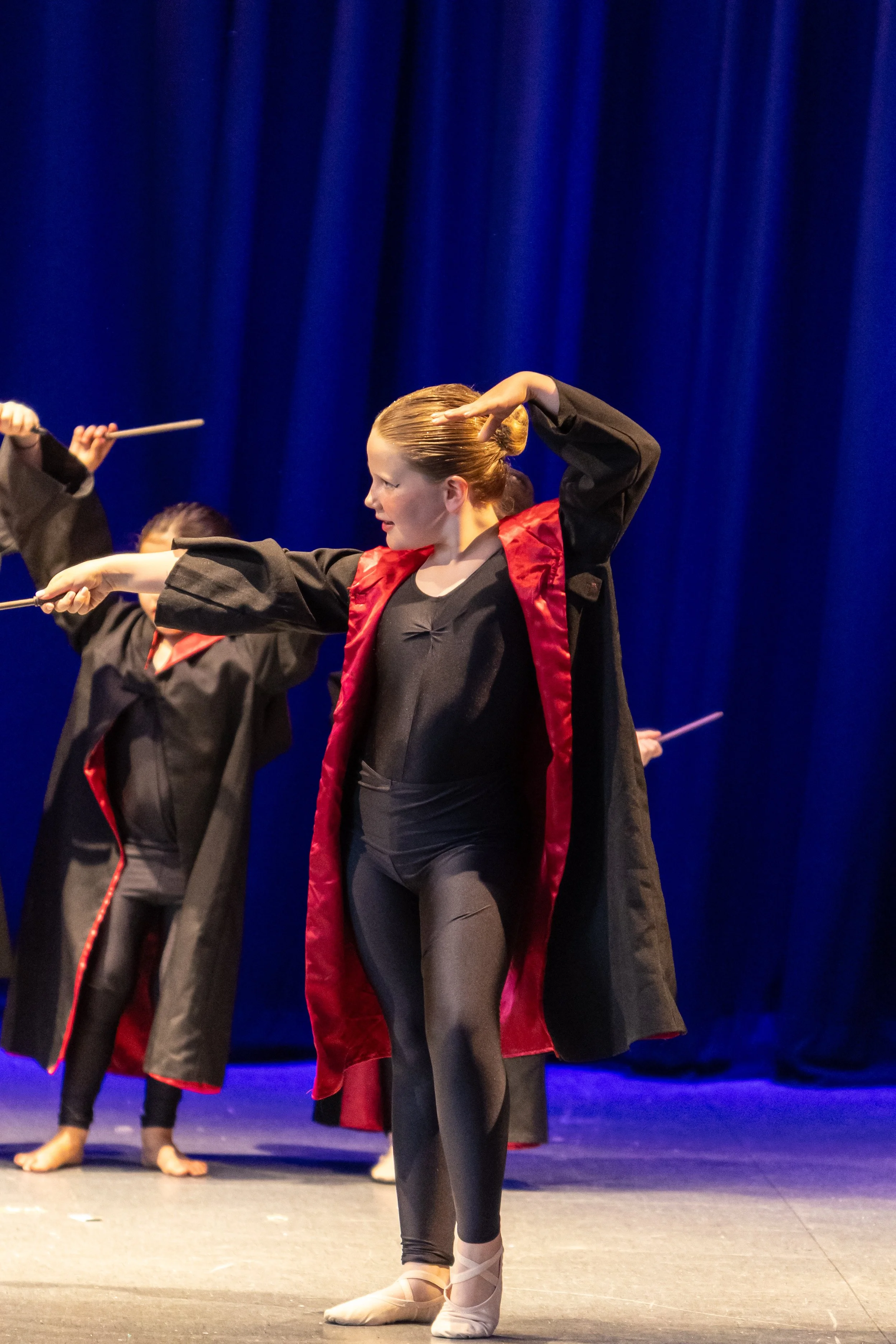 Ballet dancers performing on stage with dark blue curtains in the background.
