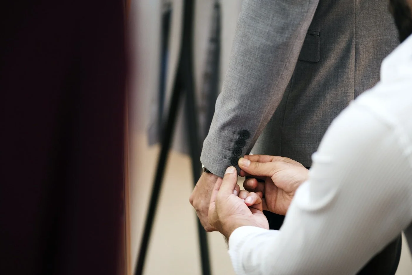 A person helping another person button a cuff on a gray suit jacket.