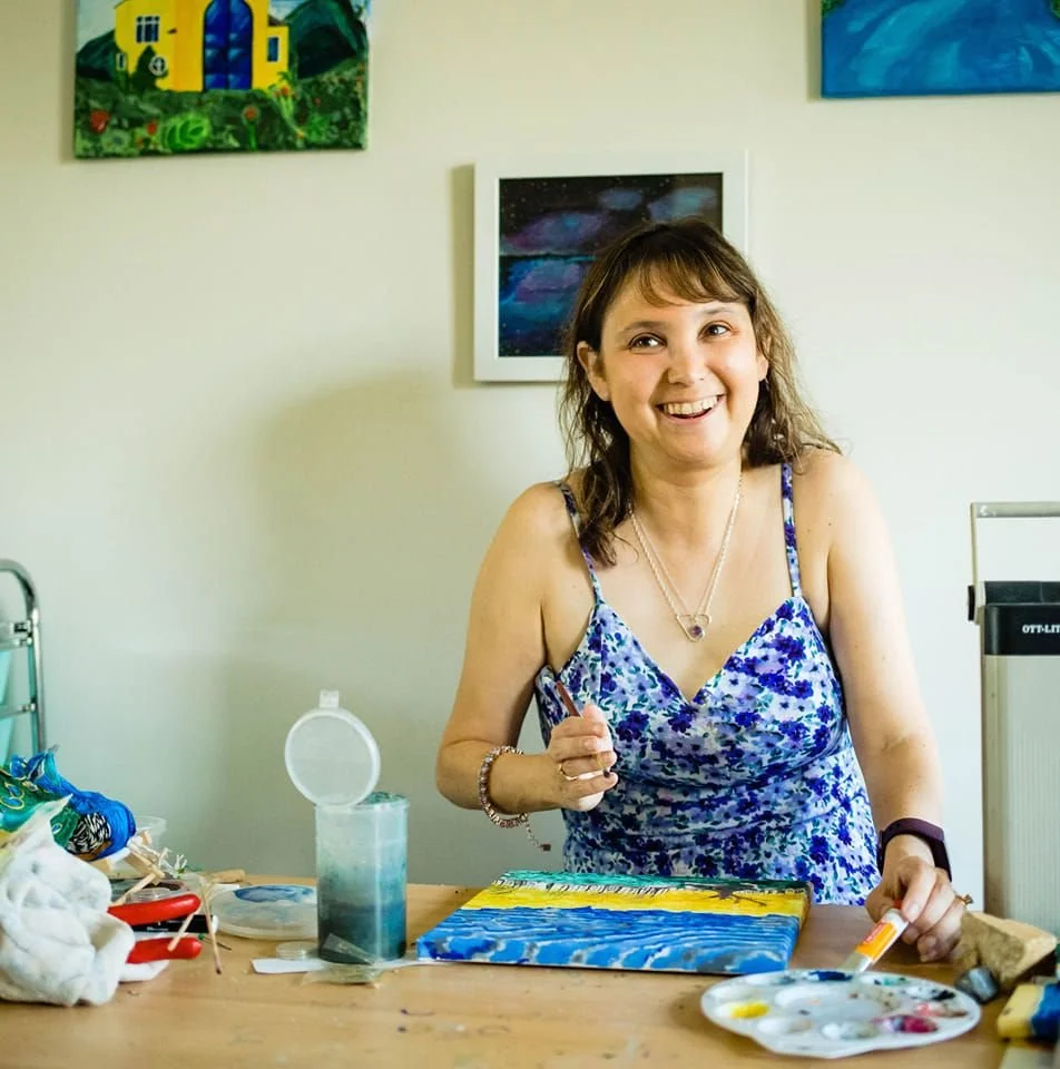 Woman holding paintbrush at a desk in front of a painting in progress