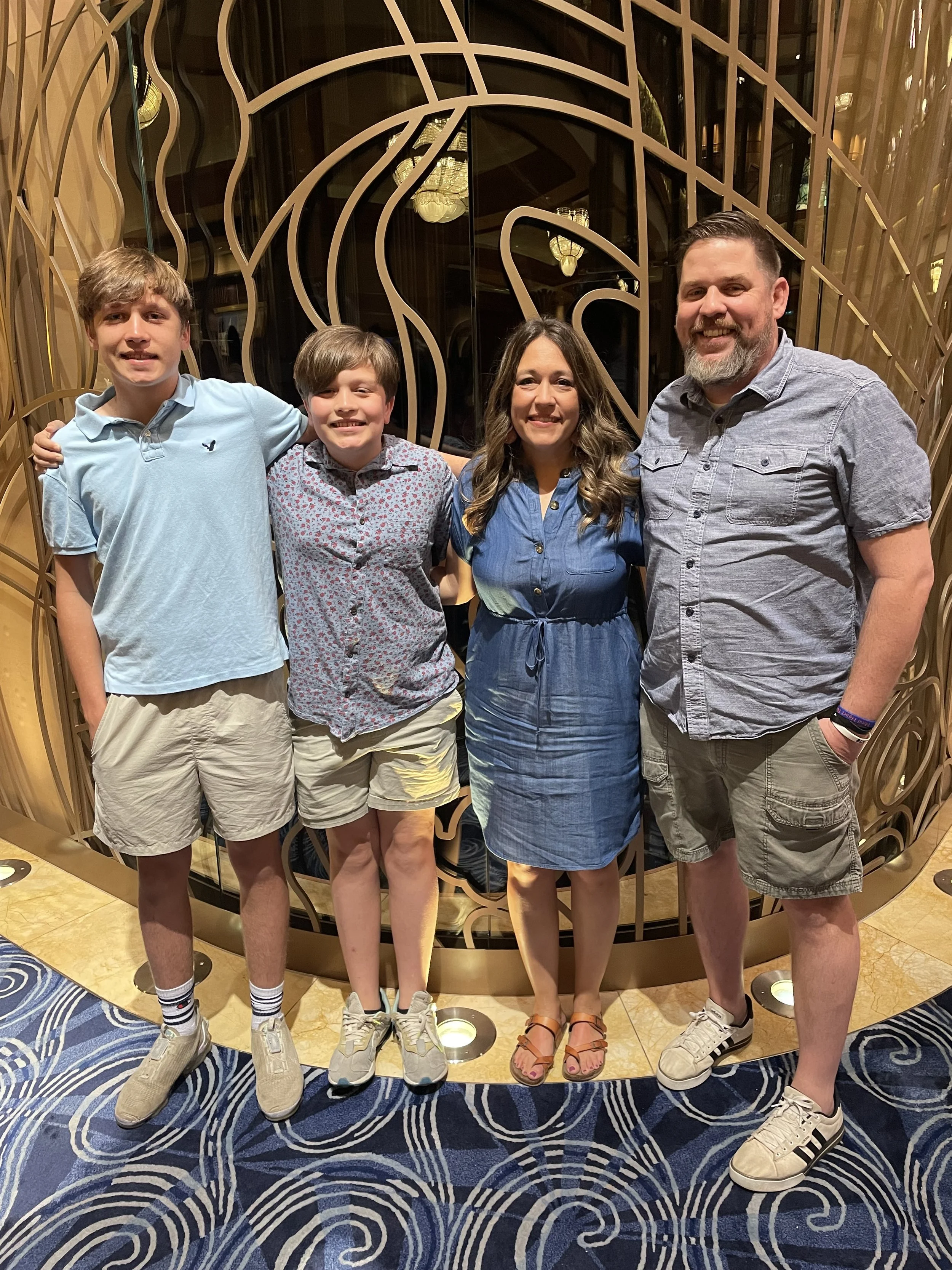 Family of four posing together, standing in front of a decorative metal screen with circular patterns on a blue carpeted floor.