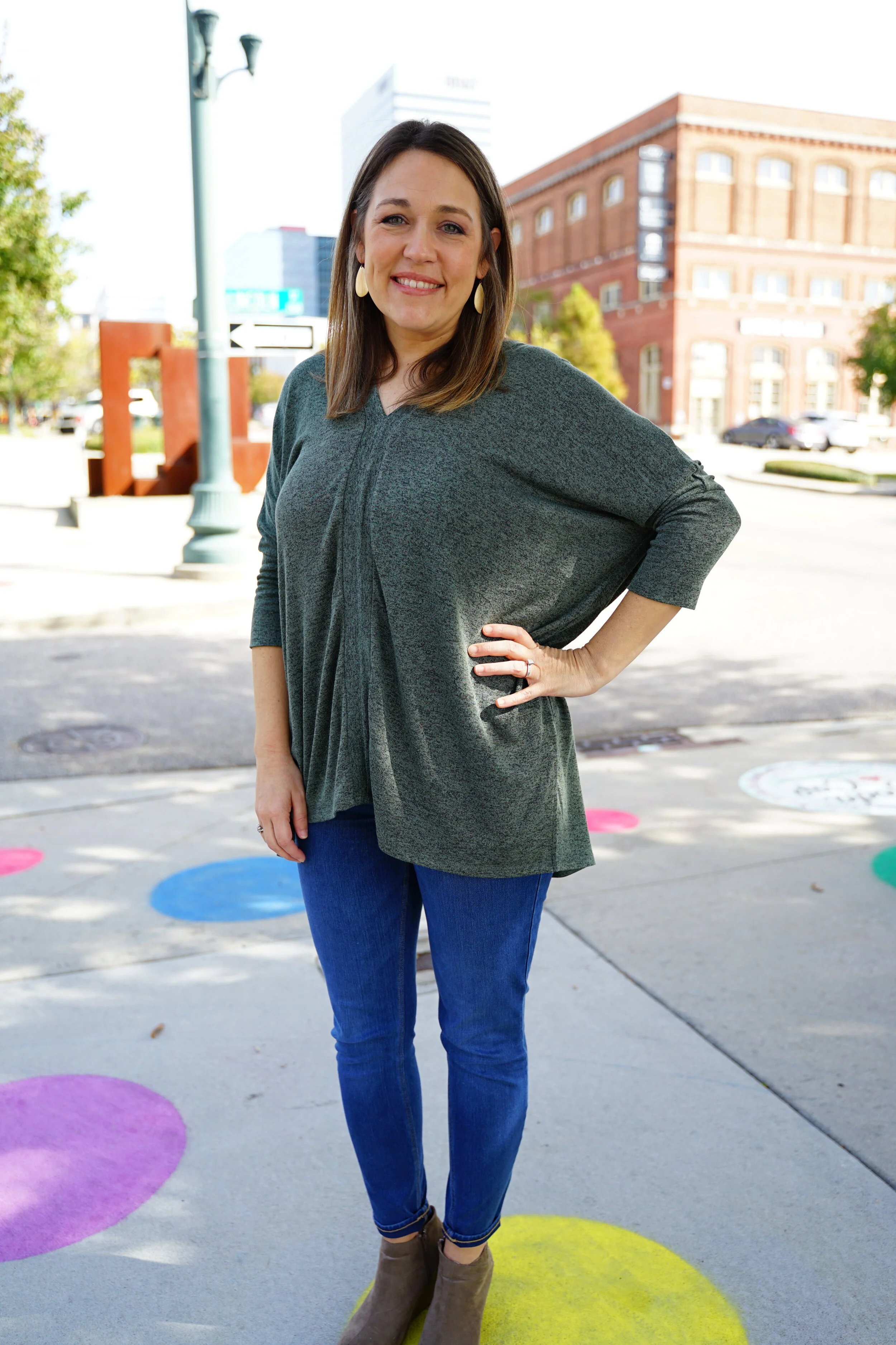 A woman standing on a city sidewalk, smiling, with one hand on her hip.