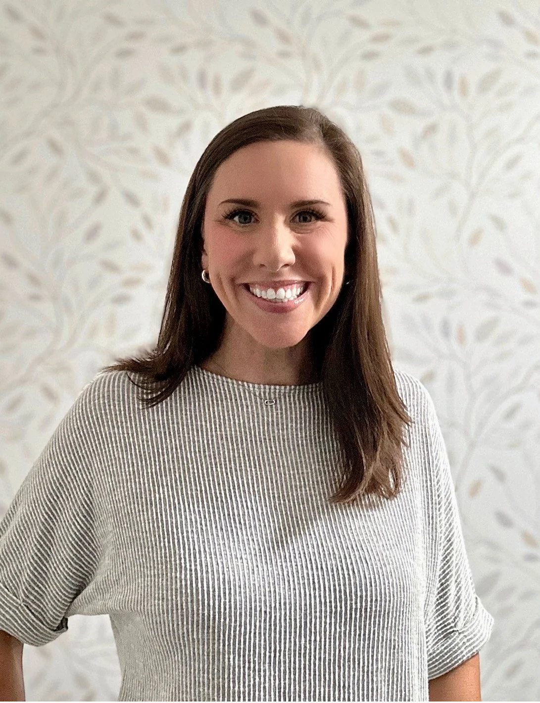 Smiling person in a striped shirt against a floral patterned background.