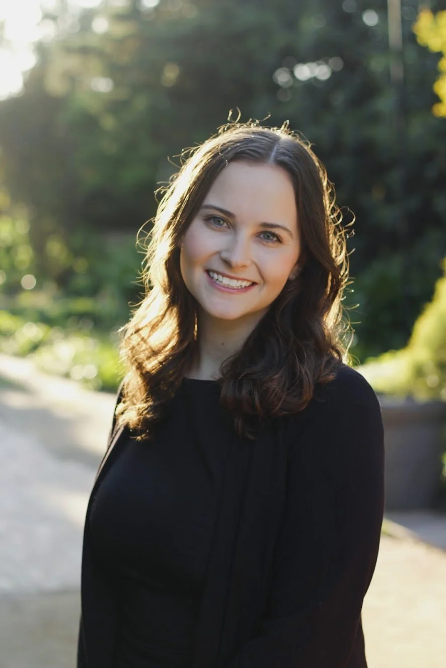A person wearing a black shirt, standing in an outdoor setting and smiling.