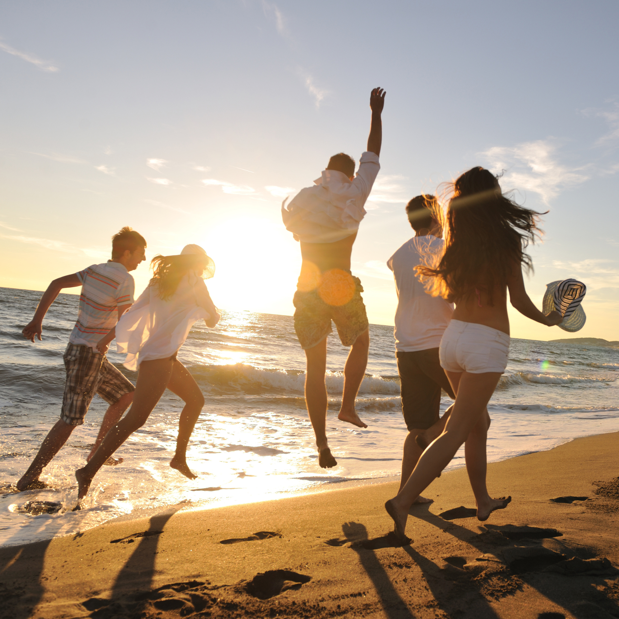 5 People running along a beach, as the sun sets.