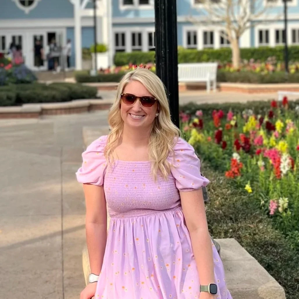 A person standing wearing a pink polka-dotted dress, in a garden setting.