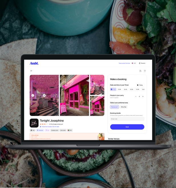 Laptop screen showing a booking page for a venue called Tonight Josephine with photos of a pink-themed exterior and interior. The background includes dishes, vegetables, and bread on a table.