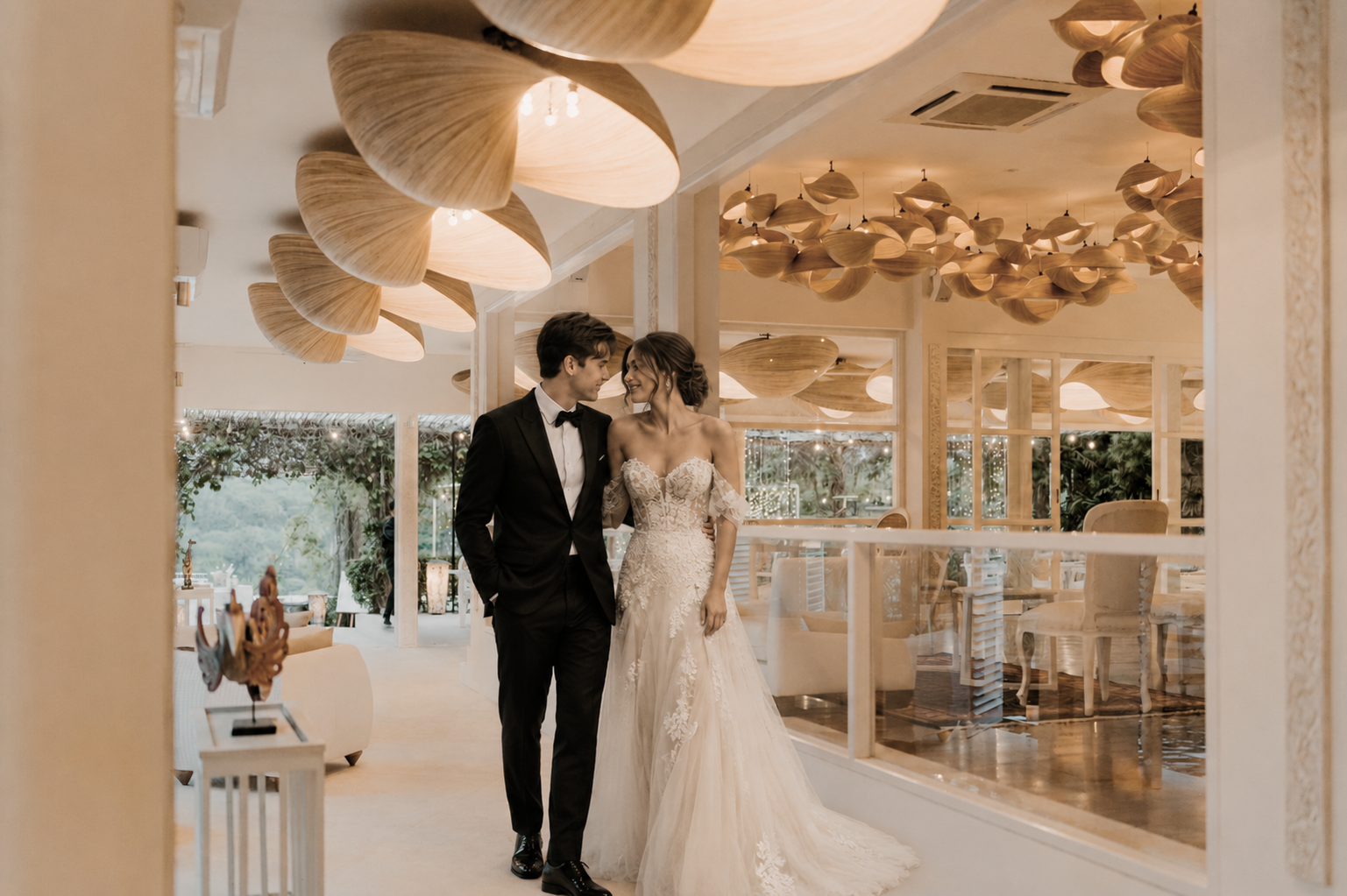 A bride and groom in wedding attire sharing a moment inside a beautifully decorated reception hall, with warm lighting and modern design elements.