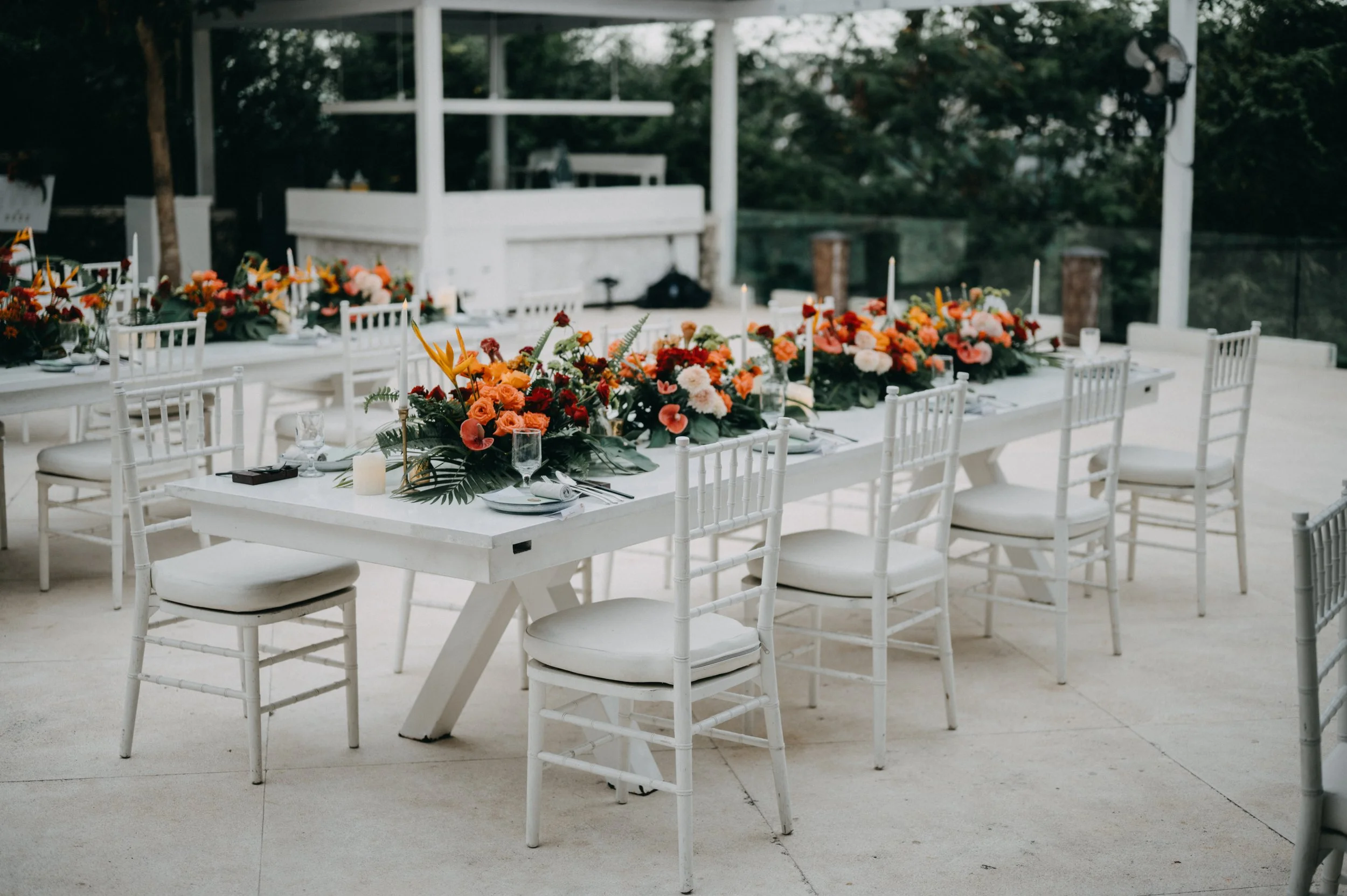 Outdoor reception setup with white tables and chairs, adorned with colorful floral centerpieces.