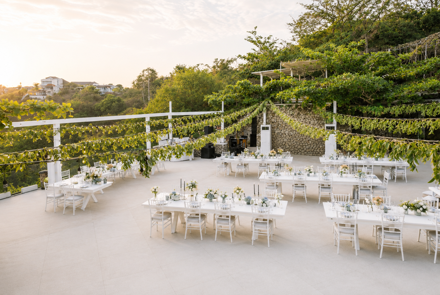 Outdoor wedding reception setup with tables, chairs, string lights, and floral decorations.