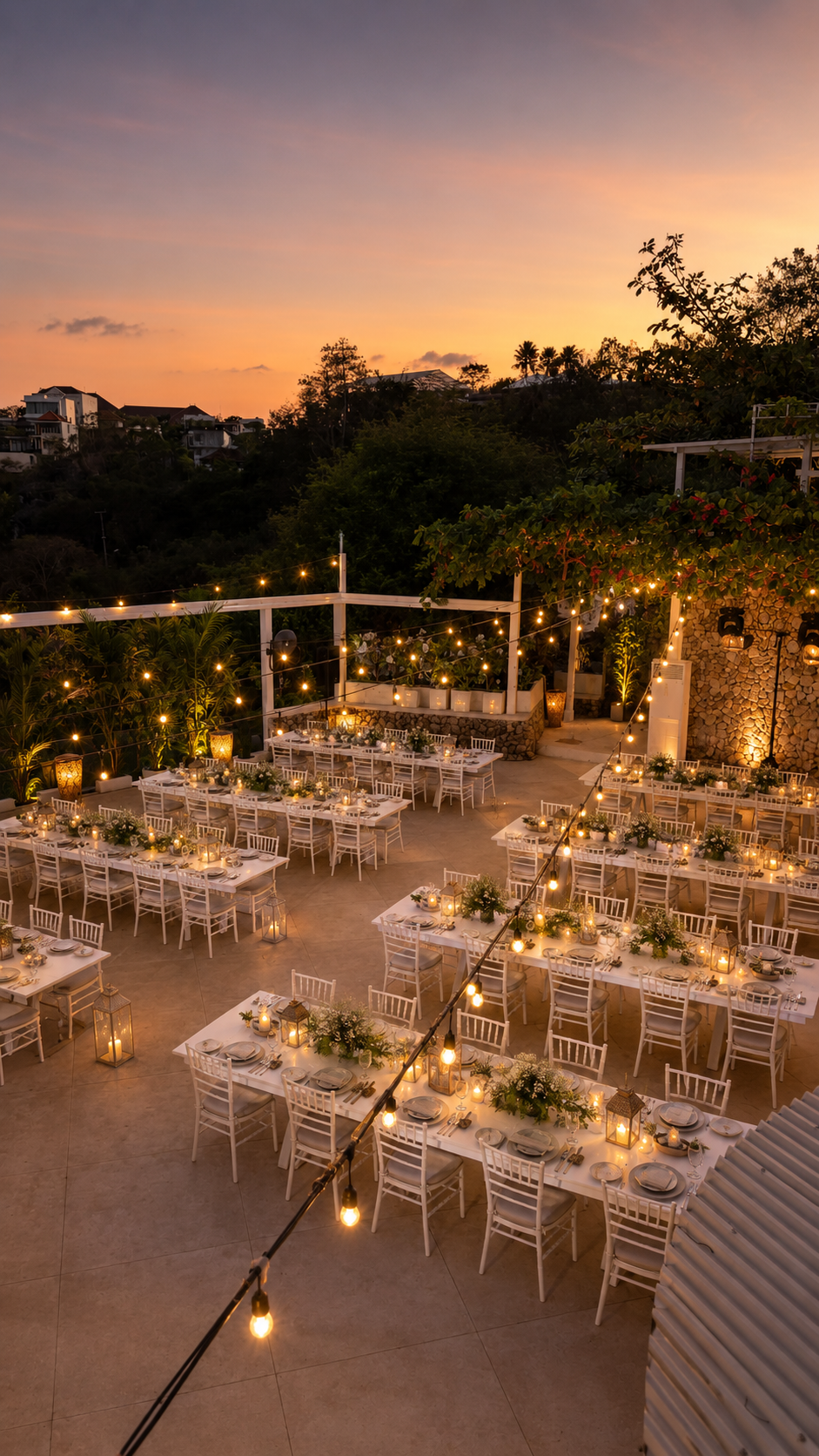 Outdoor dining area decorated with string lights and lanterns, set for a party or wedding during sunset.
