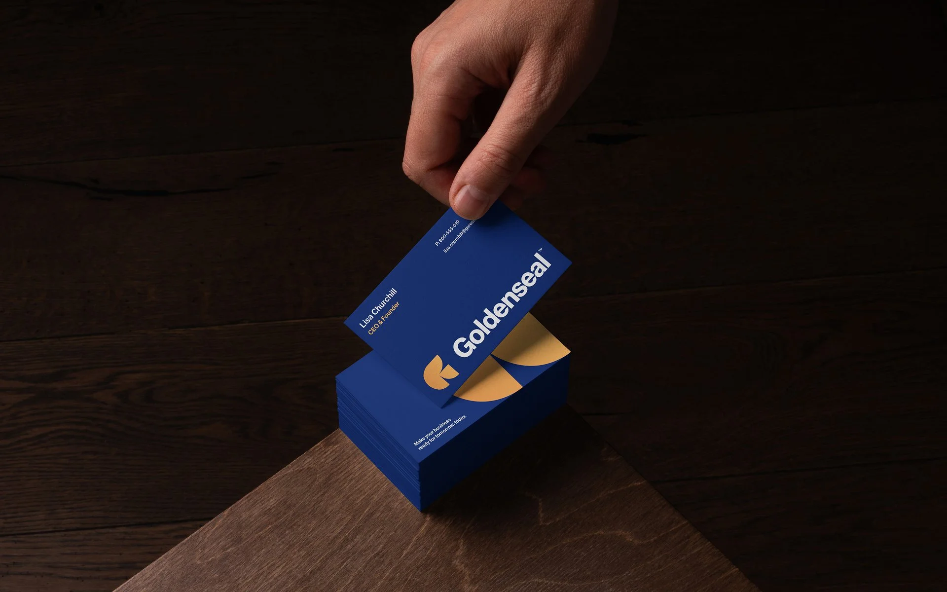 Goldenseal branded business cards with logo design being picked up from a stack on a wooden surface
