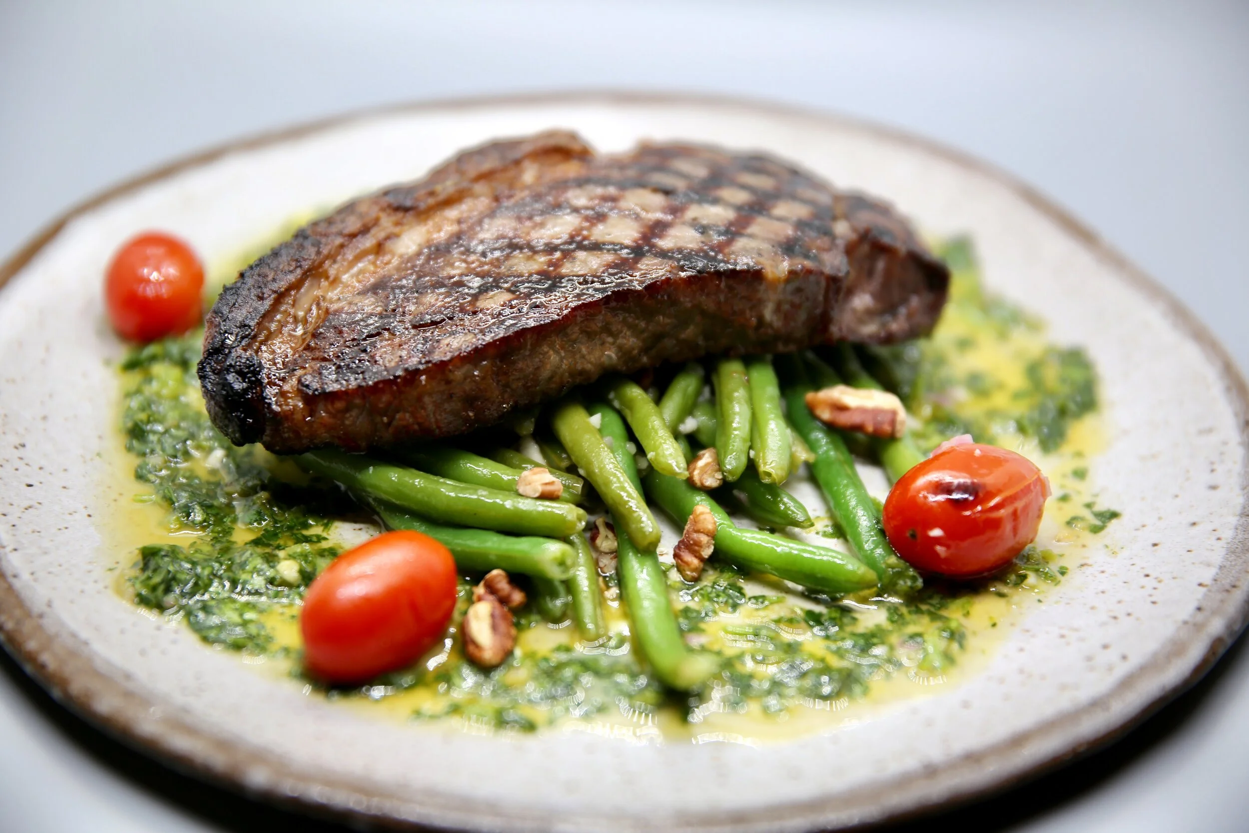 A perfectly-seared New York Strip steak on a bed of green beans, blistered cherry tomatoes and chimichurri at James Beard Award nominated East Nashville restaurant, Lockeland Table.