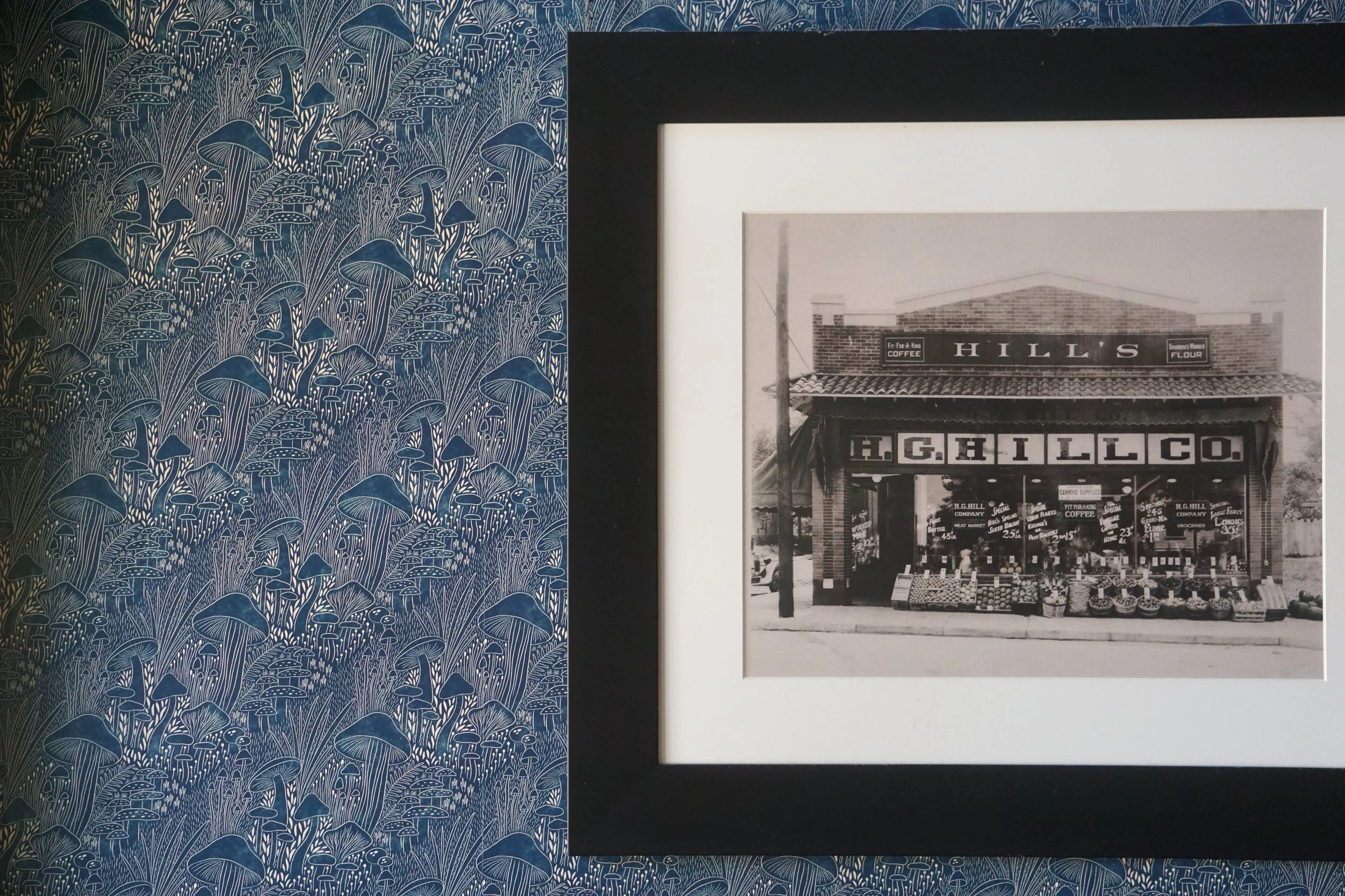  An interior wall of James Beard Award nominated East Nashville restaurant, Lockeland Table that features cozy wallpaper and a photo of a previous iteration of the building. It was an HG Hill grocery store. 
