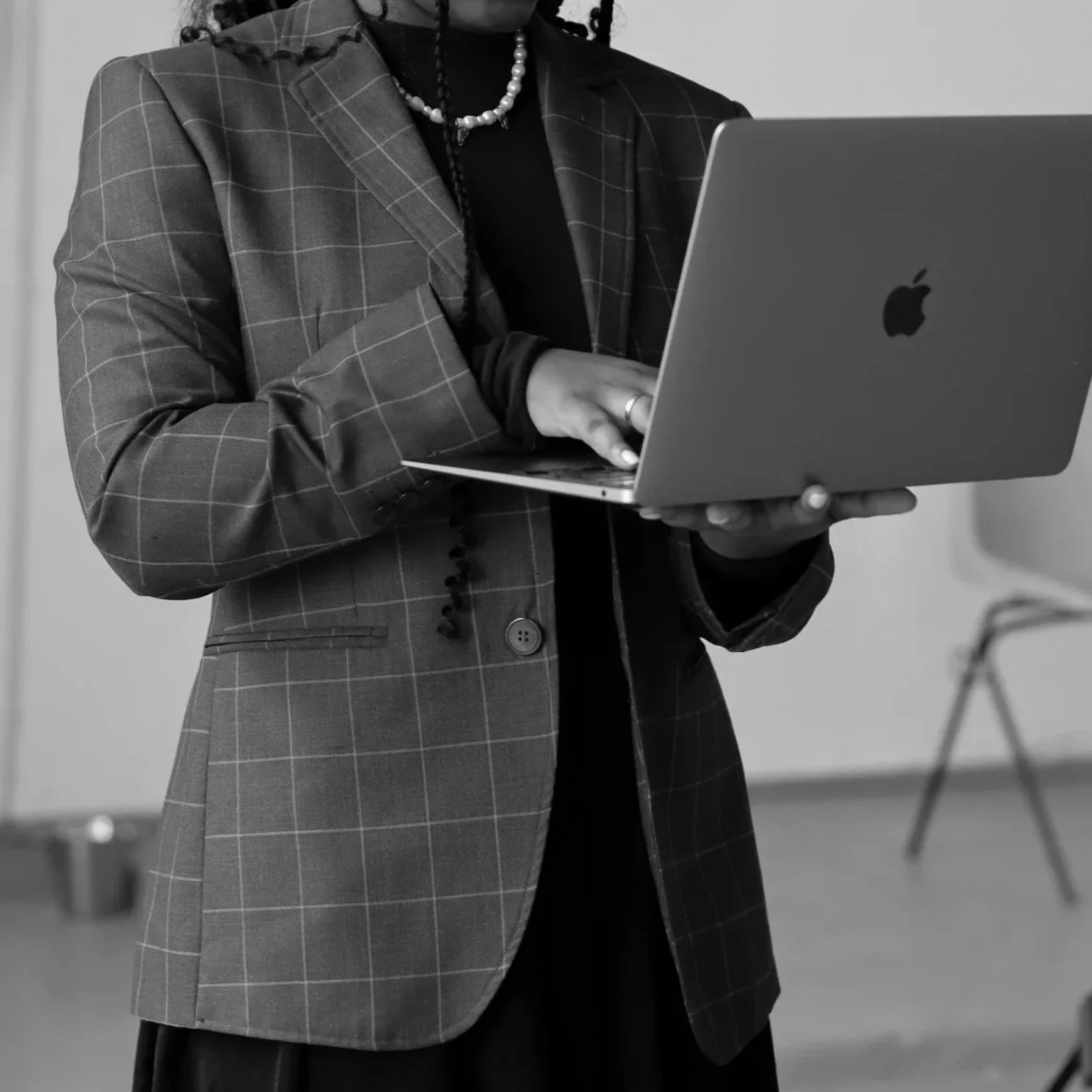 Woman in plaid blazer using a silver Apple MacBook laptop.