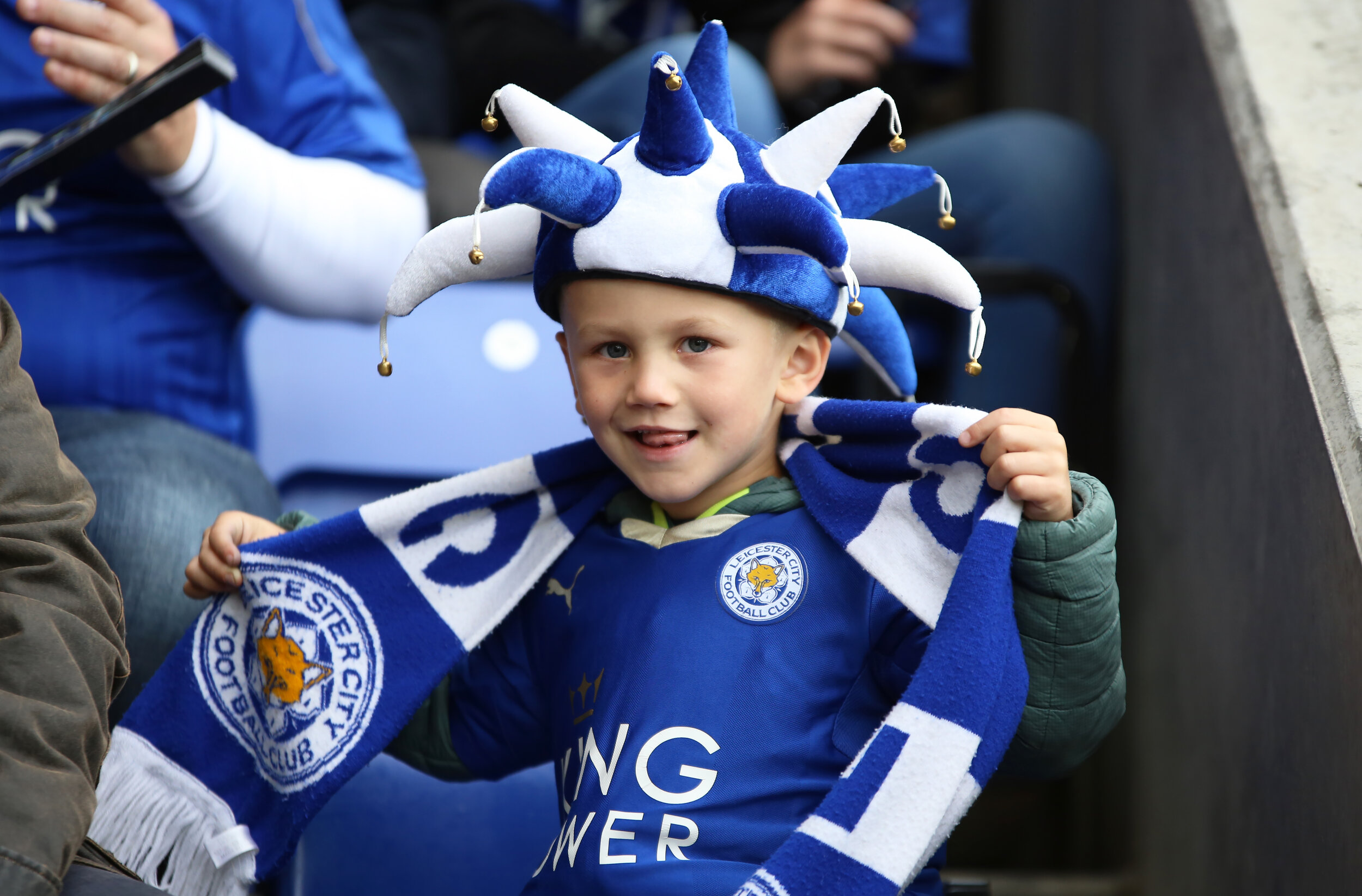 Child wearing blue jester hat and Leicester City football scarf.