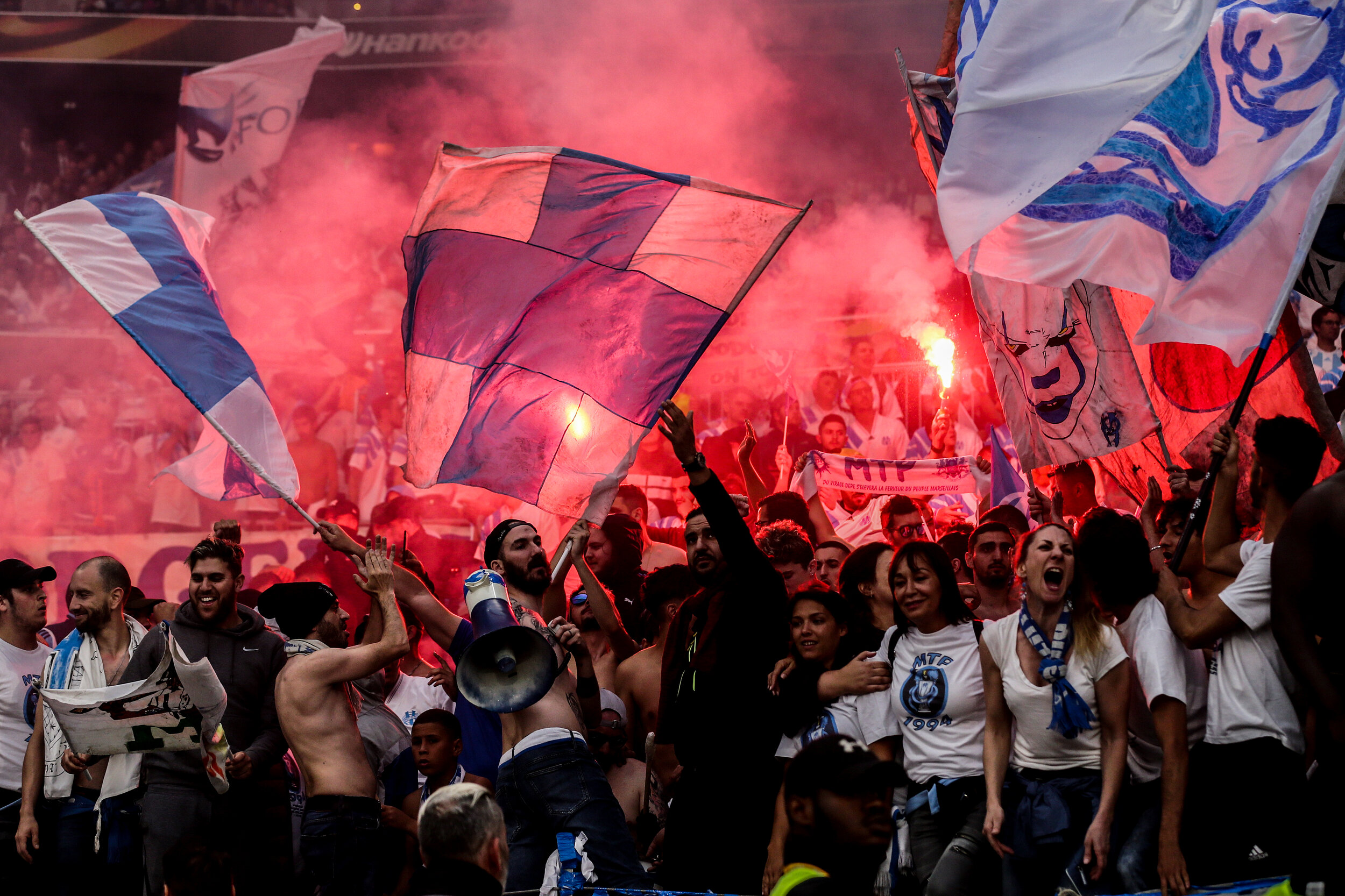 Soccer fans waving flags and celebrating with flares in a stadium.
