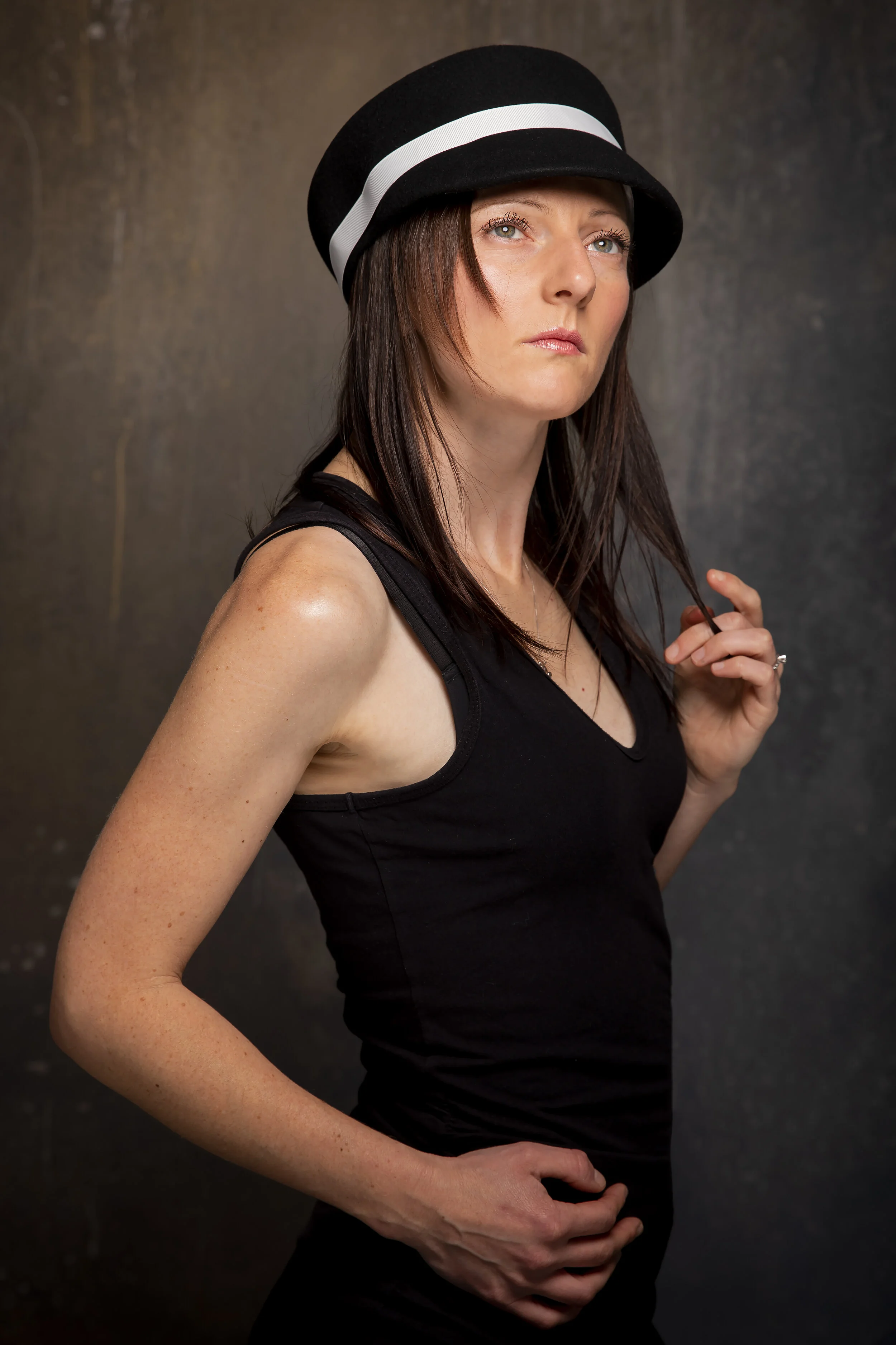 Woman in black hat and dress posing with dramatic lighting
