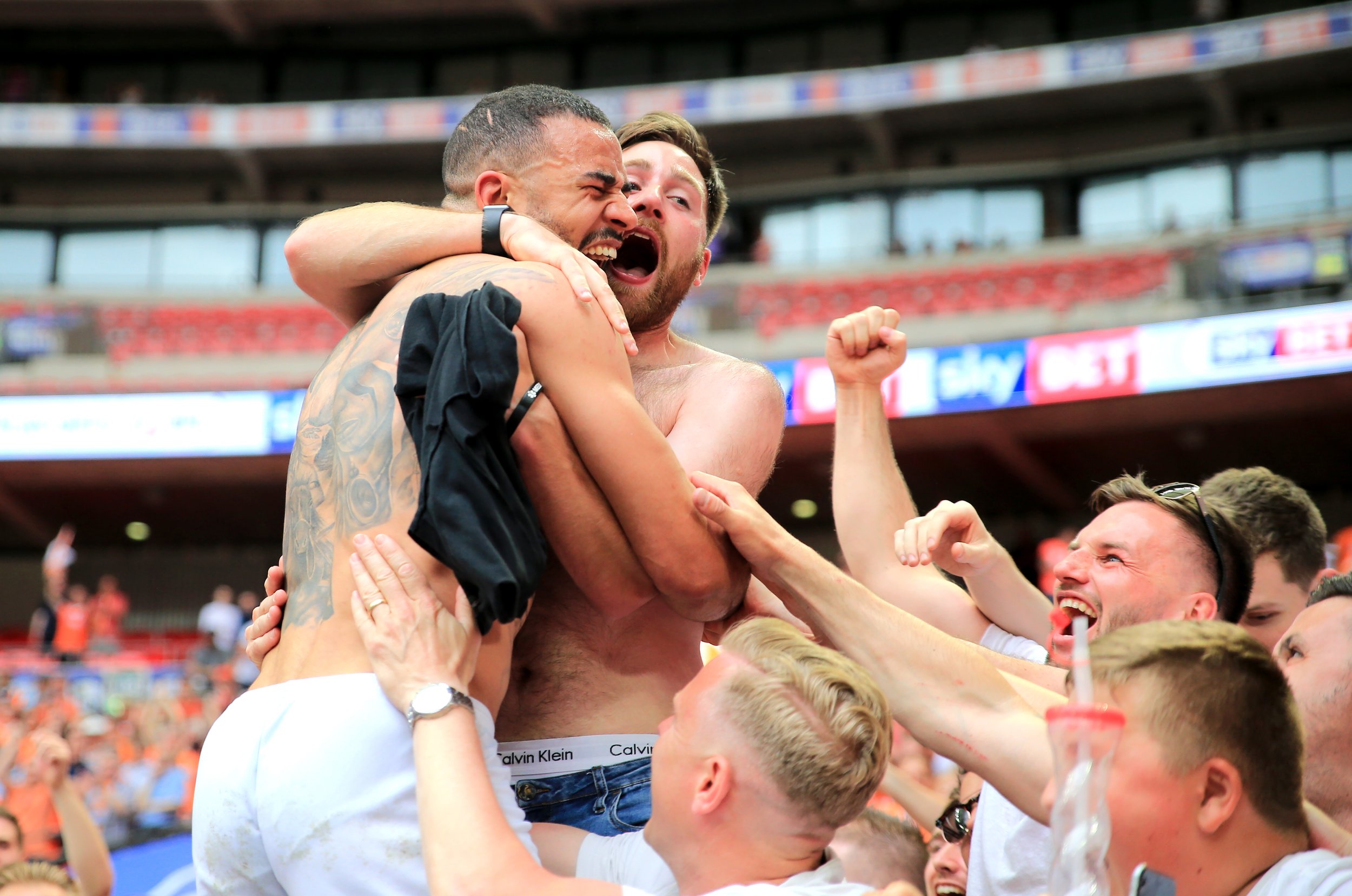Celebration at a sports event with jubilant shirtless fans hugging and cheering in a stadium.