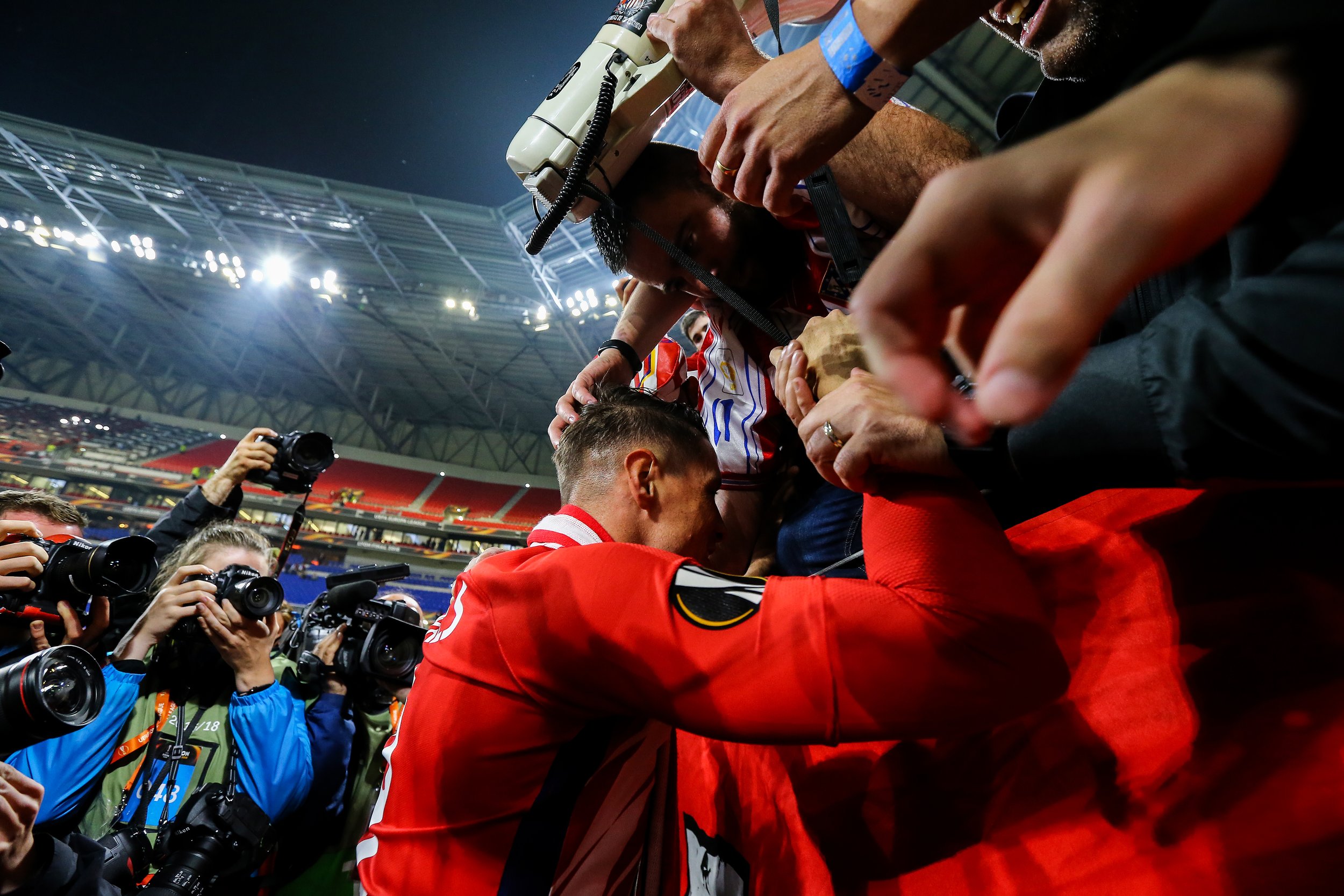 Soccer player hugging fan after match surrounded by photographers.