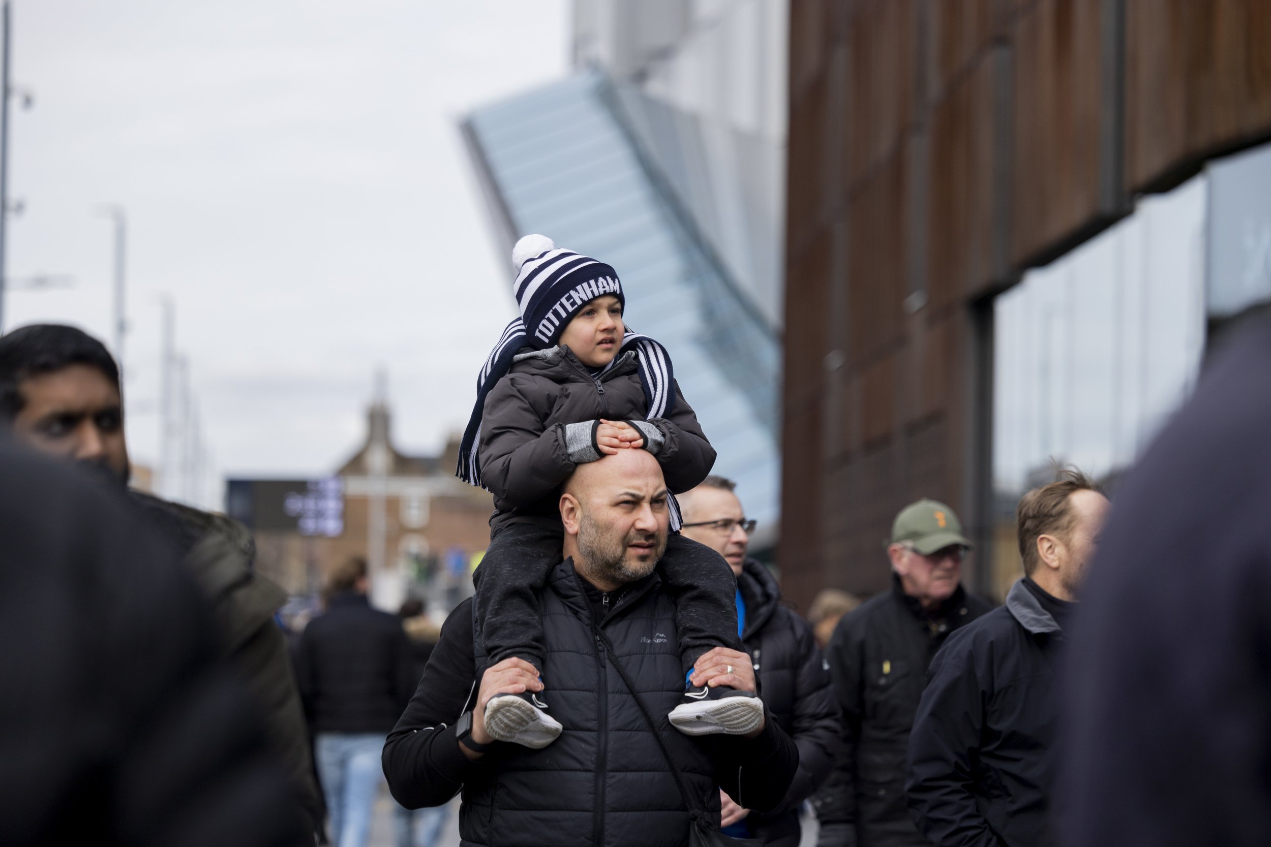A man carrying a child on his shoulders in a crowd near a modern building.