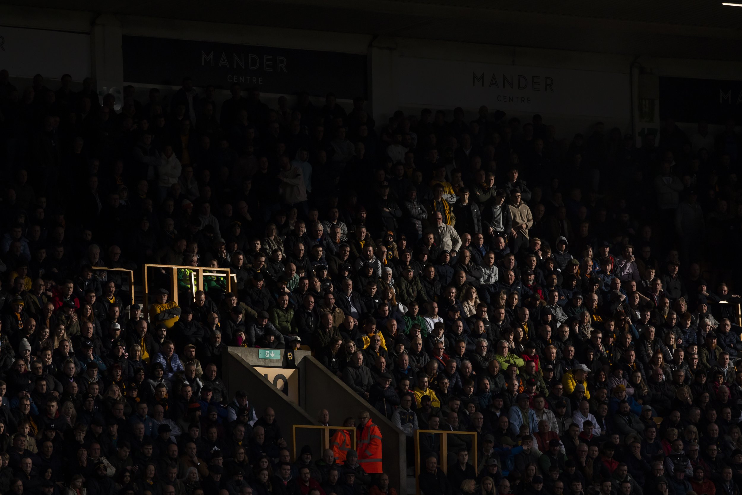 Crowd of people seated in a stadium section with dim lighting.