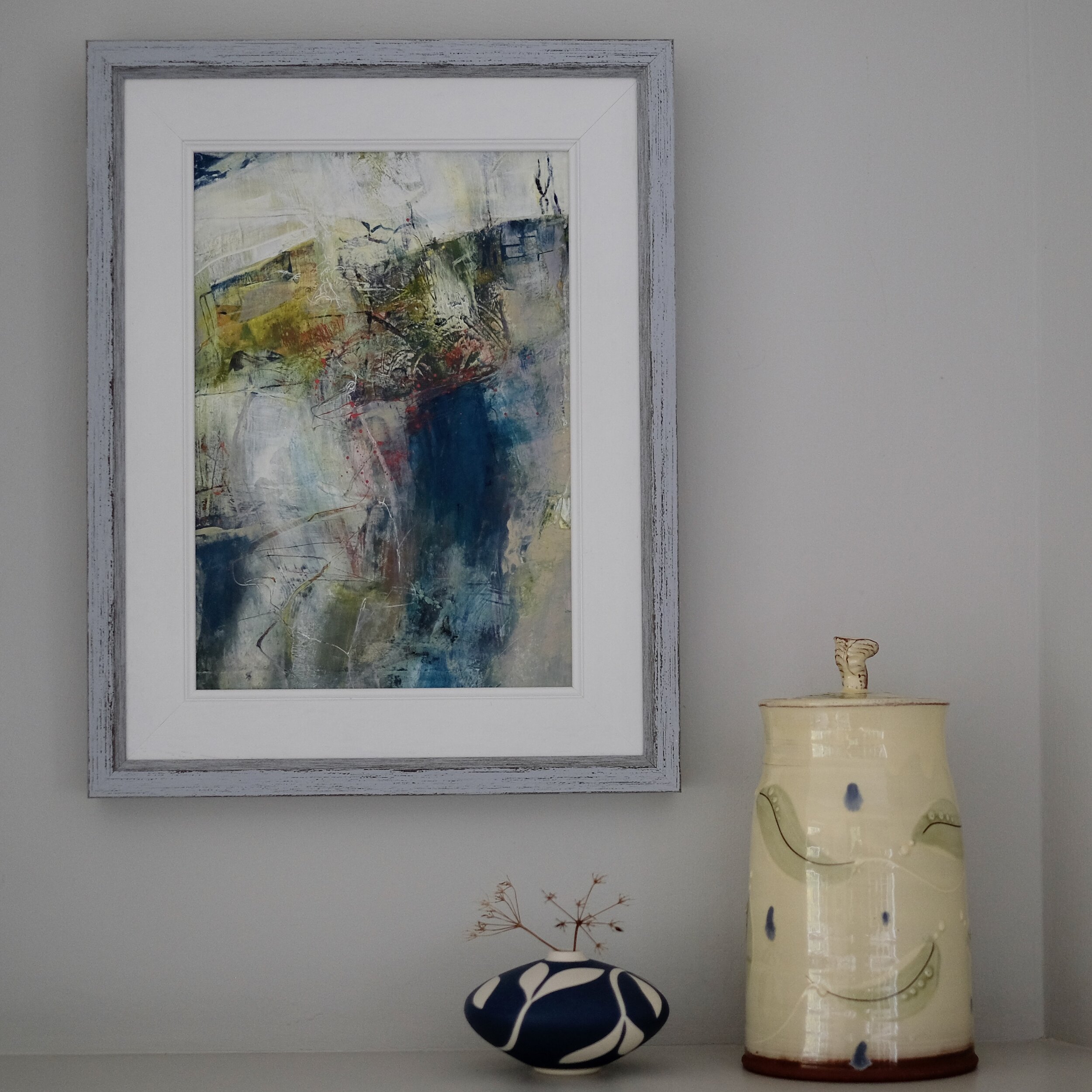 Framed multicoloured abstract acrylic painting by Joanne Olney displayed with small vase and ceramic pot