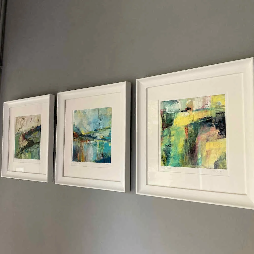 3 white framed abstract paintings by Joanne Olney of a multi coloured landscapes