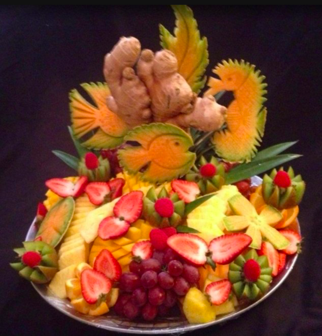 Fruit platter decorated with carved fruits, ginger, and seahorse-shaped fruit carvings, featuring strawberries, grapes, pineapple, and kiwi.