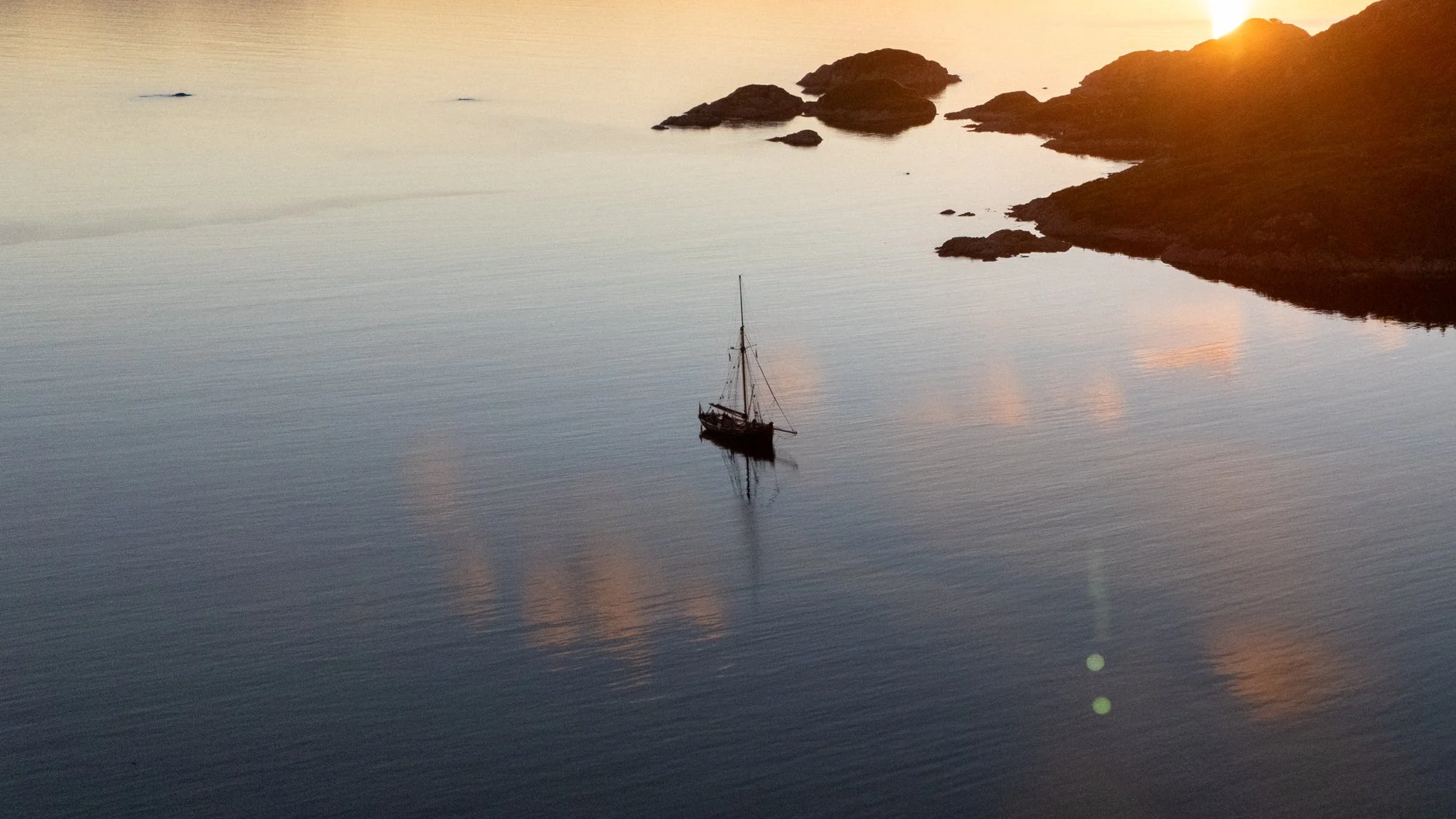 Sailboat on calm water near rocky islands at sunset.