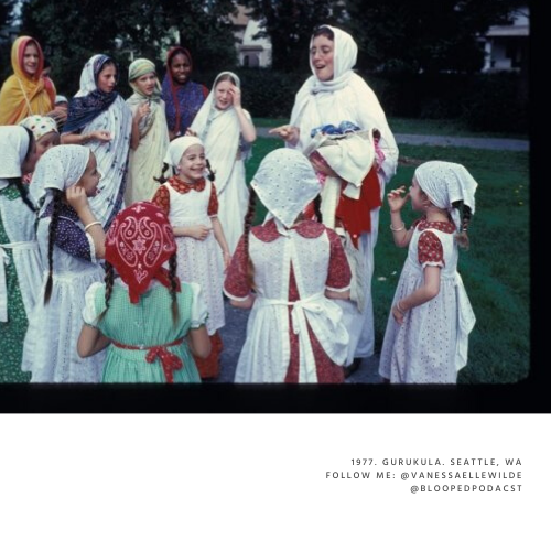 A woman dressed as Jesus with a white robe and head covering speaks to a group of children wearing traditional costumes, some with headscarves, outdoors in a park or grassy area during daytime.