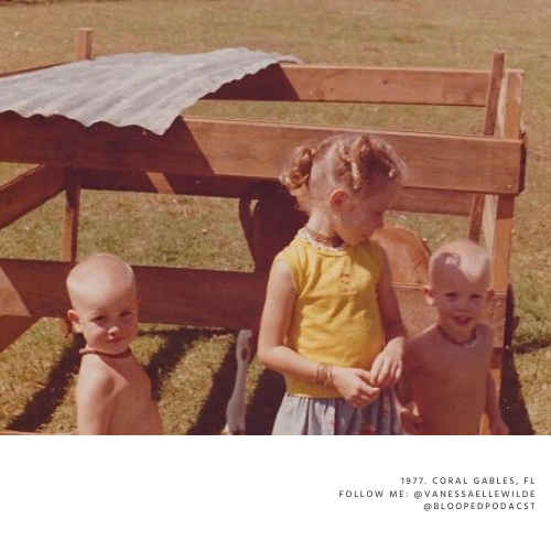 Two young children and a girl posing outdoors in front of a wooden structure, with a metal sheet on top, in a grassy area.