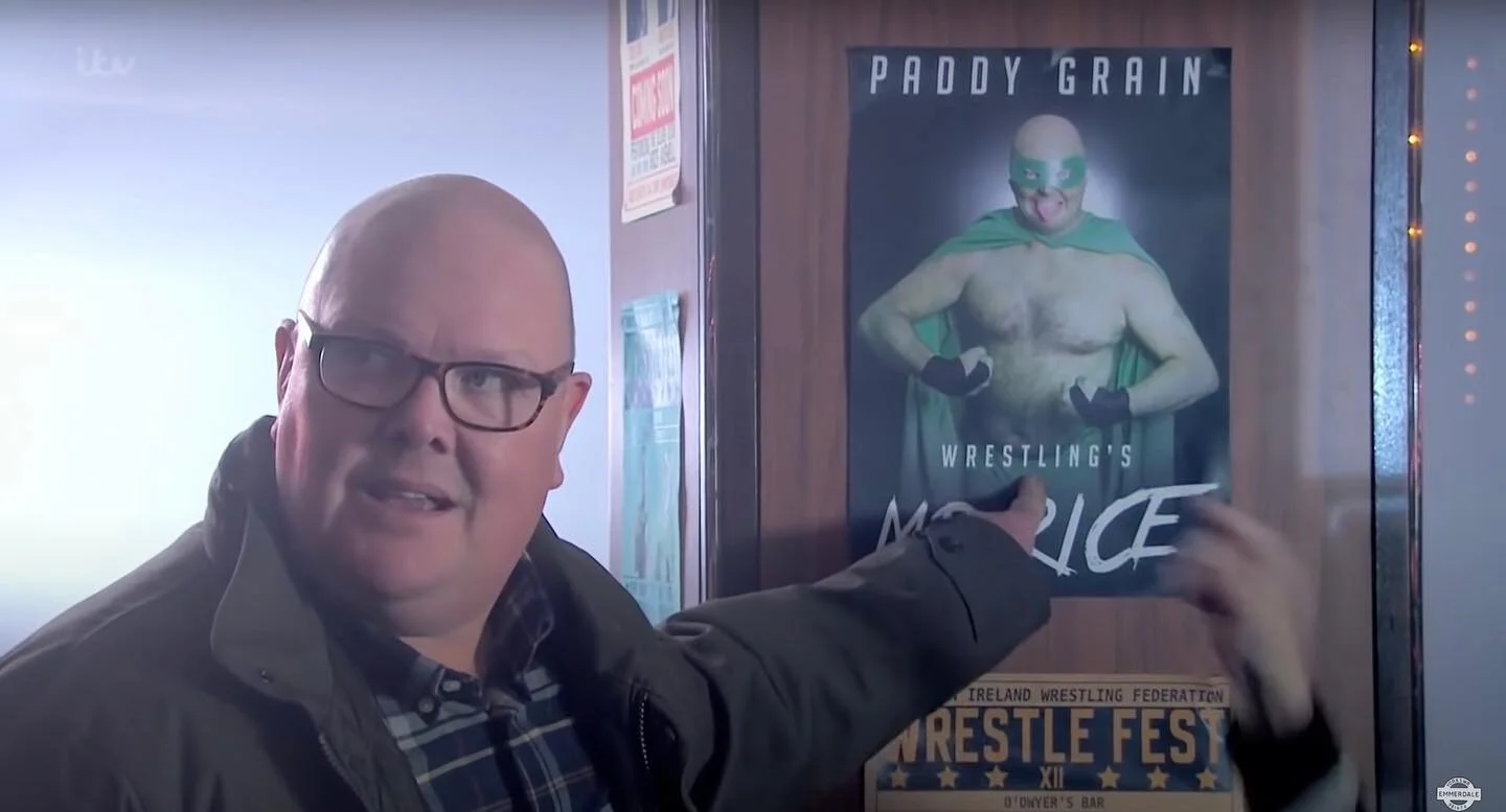 #emmerdale 

[ID Paddy is a chubby bald white man and he&rsquo;s pointing at a poster of a wrestler who is also a chubby bald white man. Paddy looks offended by the comparison. ]