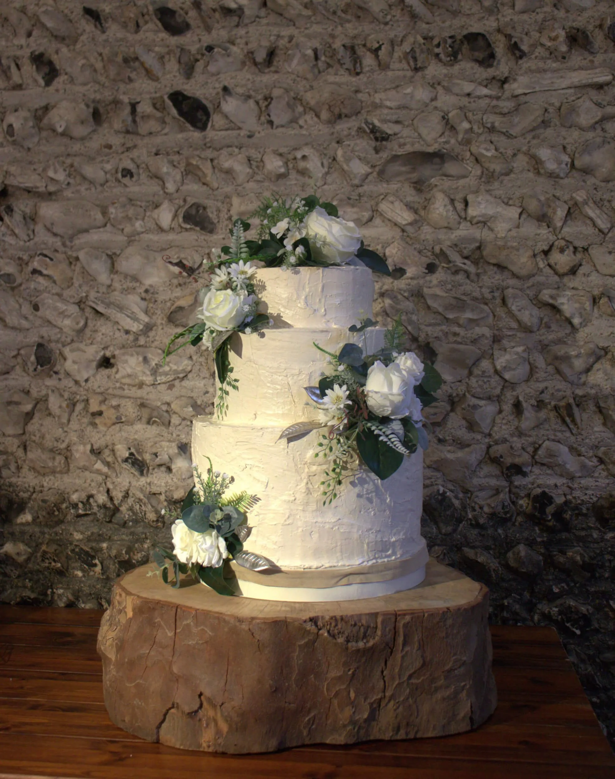 Log slice cake stand supporting a white tiered wedding cake with floral decorations, available to hire for your wedding or event.
