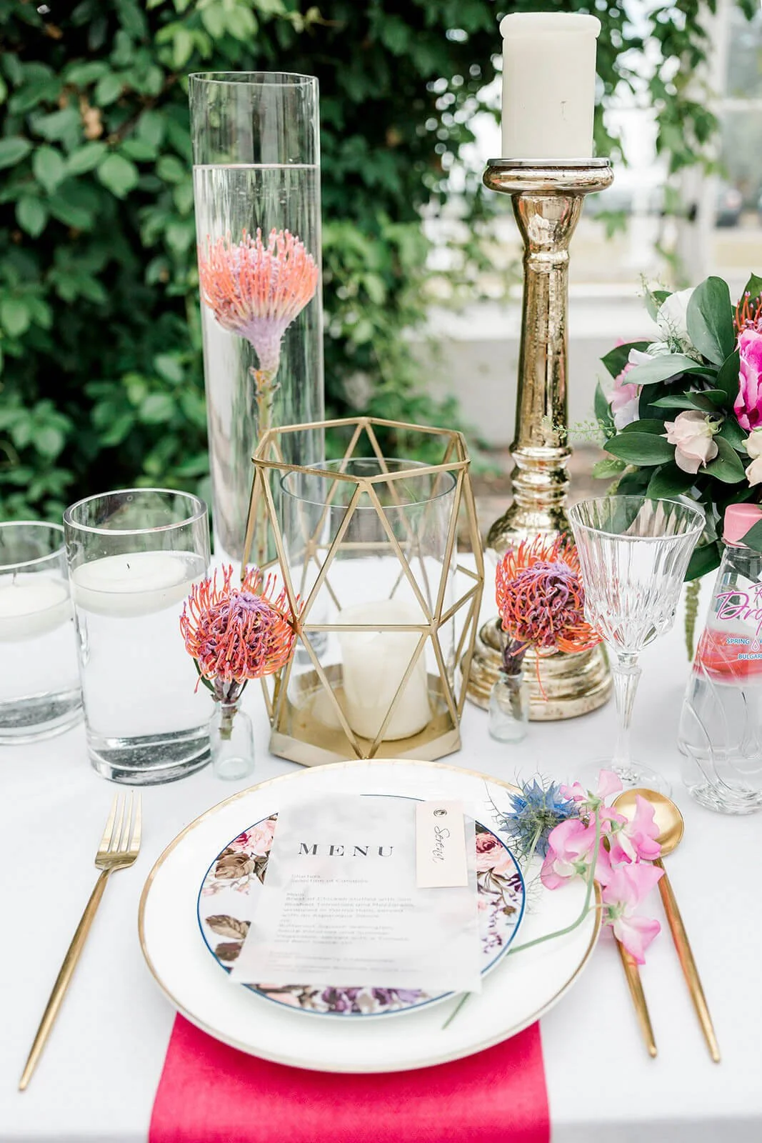 Geo Hurricane Lantern - Gold with white candle inside, styled on a wedding table with floral plates and pink flowers, available to hire for your wedding or event.