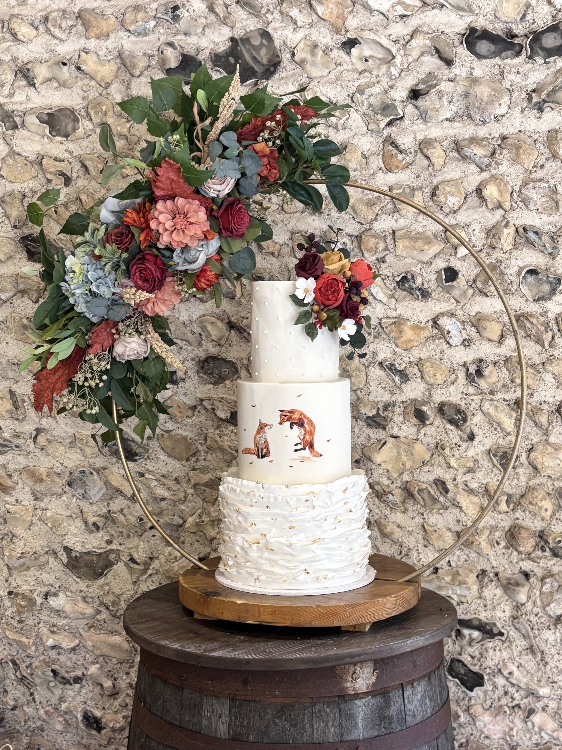 Gold Cake Stand - Hoop - 80cm hoop, 45cm base with floral decoration holding a three-tier wedding cake, available to hire for your wedding or event.