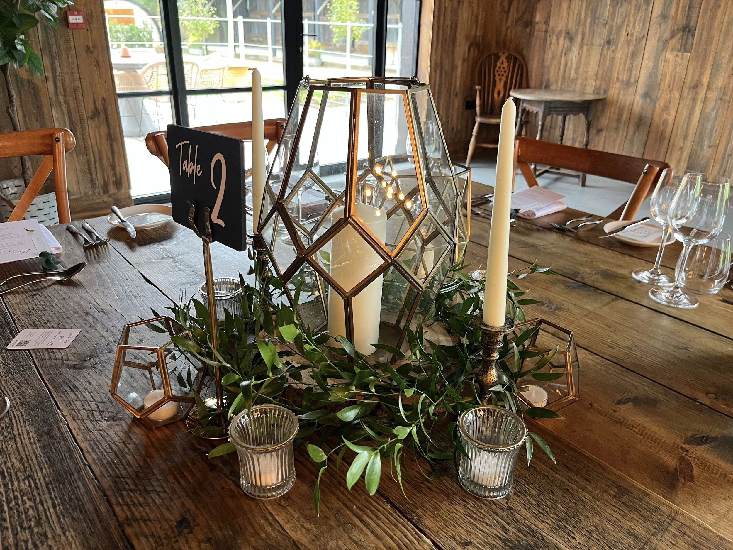 Bronze Candlestick - Small - 13cm H holding a white taper candle on a rustic wooden table, available to hire for your wedding or event.