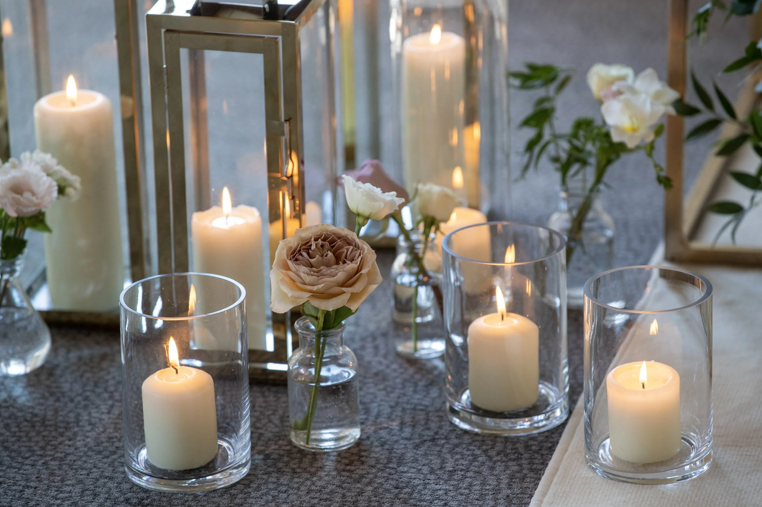 Cylinder Vase - 15cm with white pillar candles inside, available to hire for your wedding or event, styled with small glass bottles and flowers.